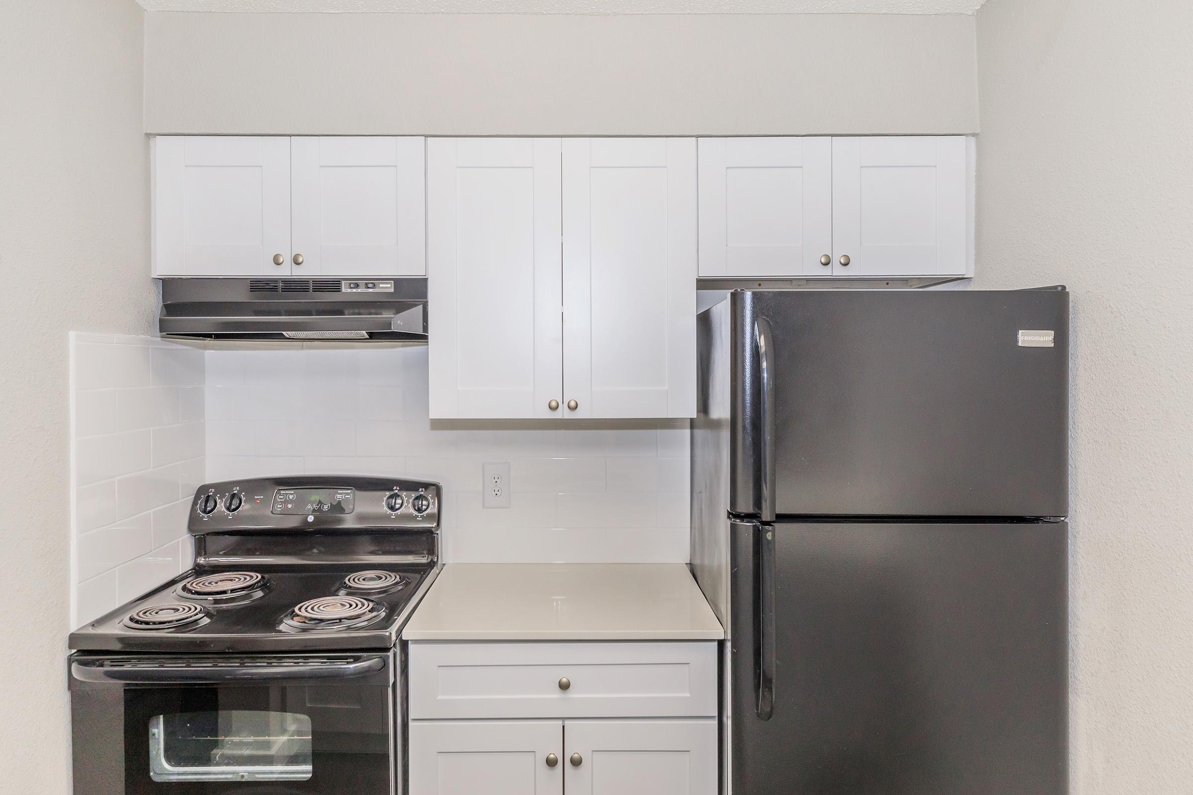 A modern kitchen featuring white cabinets, a black stove, and a black refrigerator. The stove has four burners, and the countertop is a light color. The kitchen has a sleek, clean design with a minimalist aesthetic.