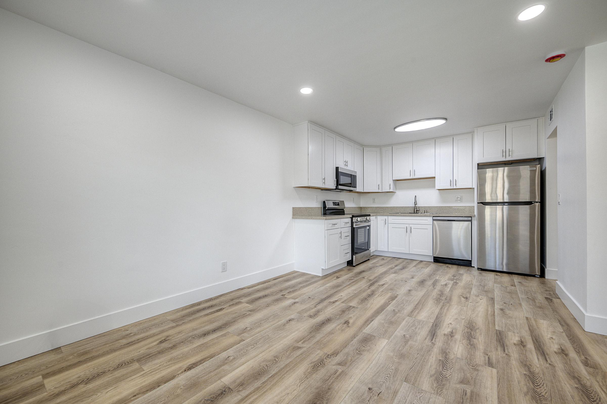 A modern kitchen featuring white cabinets, stainless steel appliances, and a light-colored countertop. The flooring is light wood, and the space is well-lit with overhead lighting. The layout is open and spacious, creating a contemporary, inviting atmosphere.