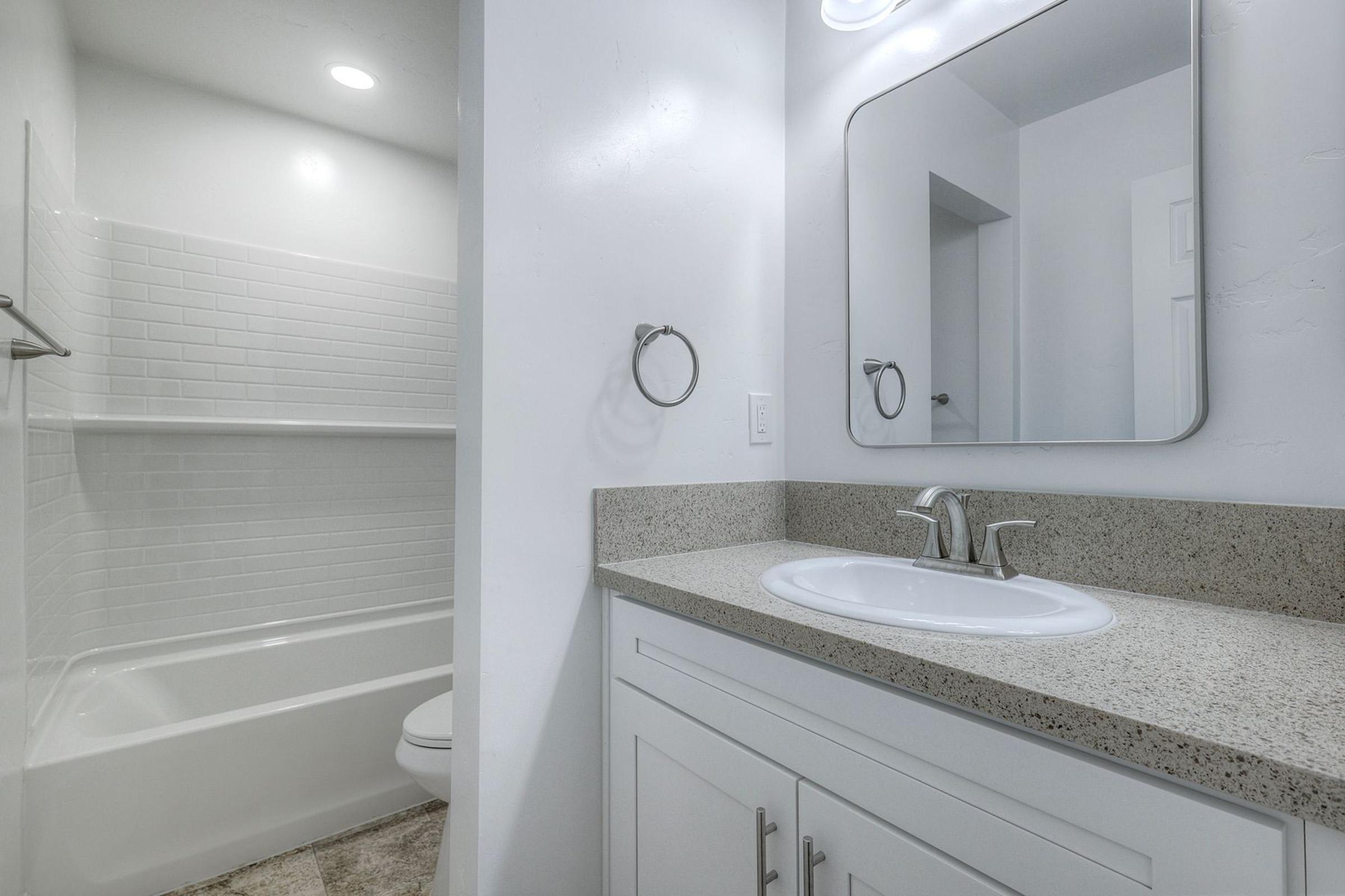 A modern bathroom featuring a white bathtub and shower combination, a sleek countertop with a sink, and a large wall-mounted mirror. The walls are painted in neutral tones, and the space is well-lit with overhead lighting.