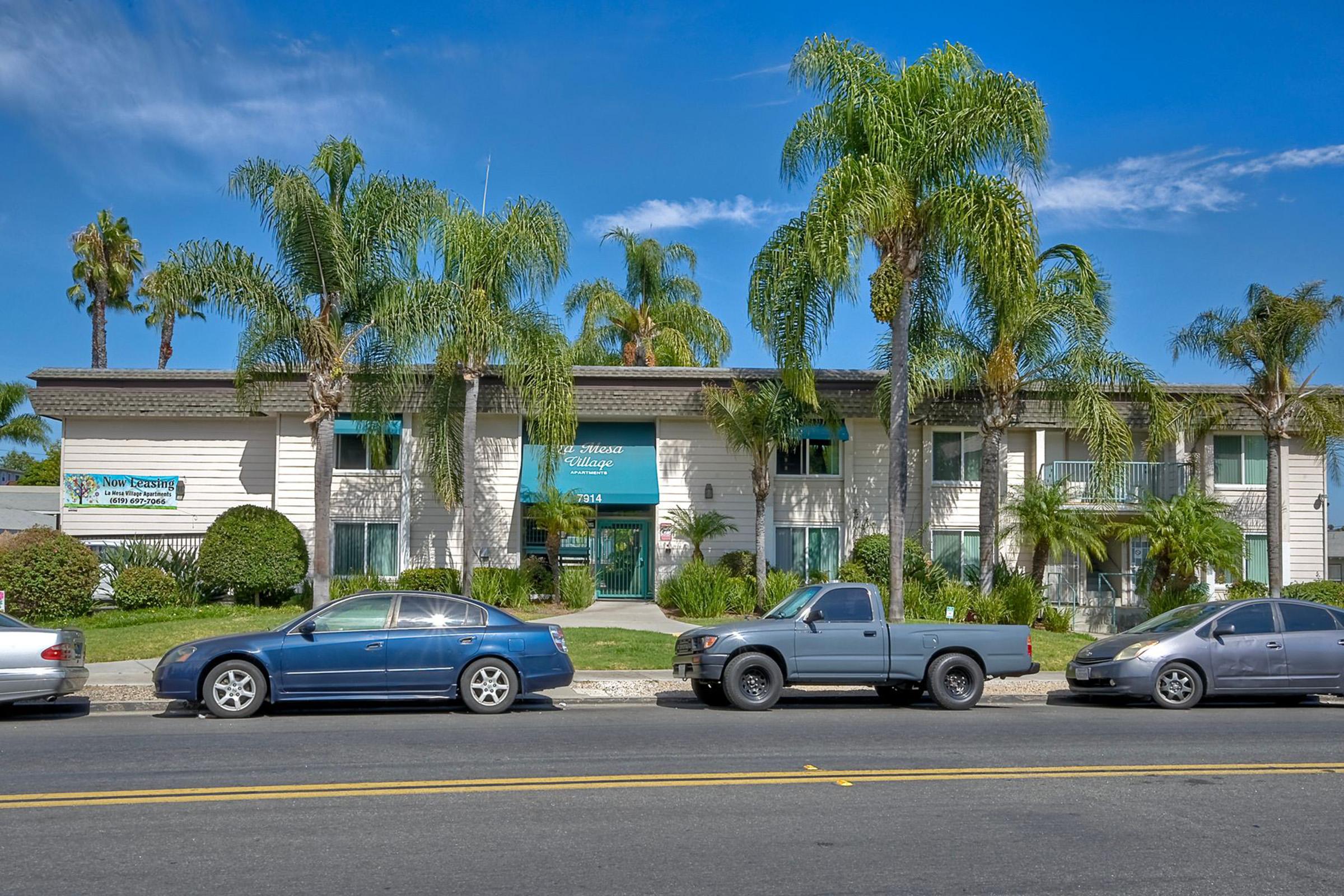 A two-story building with palm trees in front, featuring a sign that reads "Palm Coast Medical Clinic." There are several parked cars along the street, and a clear blue sky is visible in the background. The setting appears to be a sunny day in a tropical location.