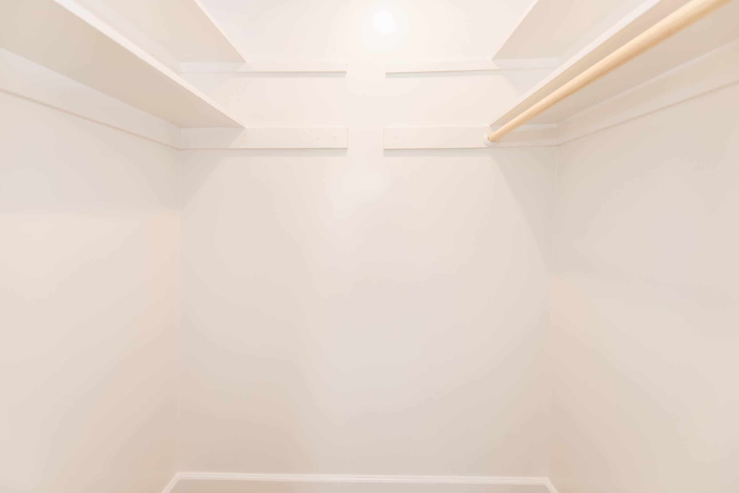 Empty closet with plain white walls and a single wooden clothing rod mounted on the back wall. The space is well-lit, highlighting the simplicity of the design and the absence of shelves or any items.