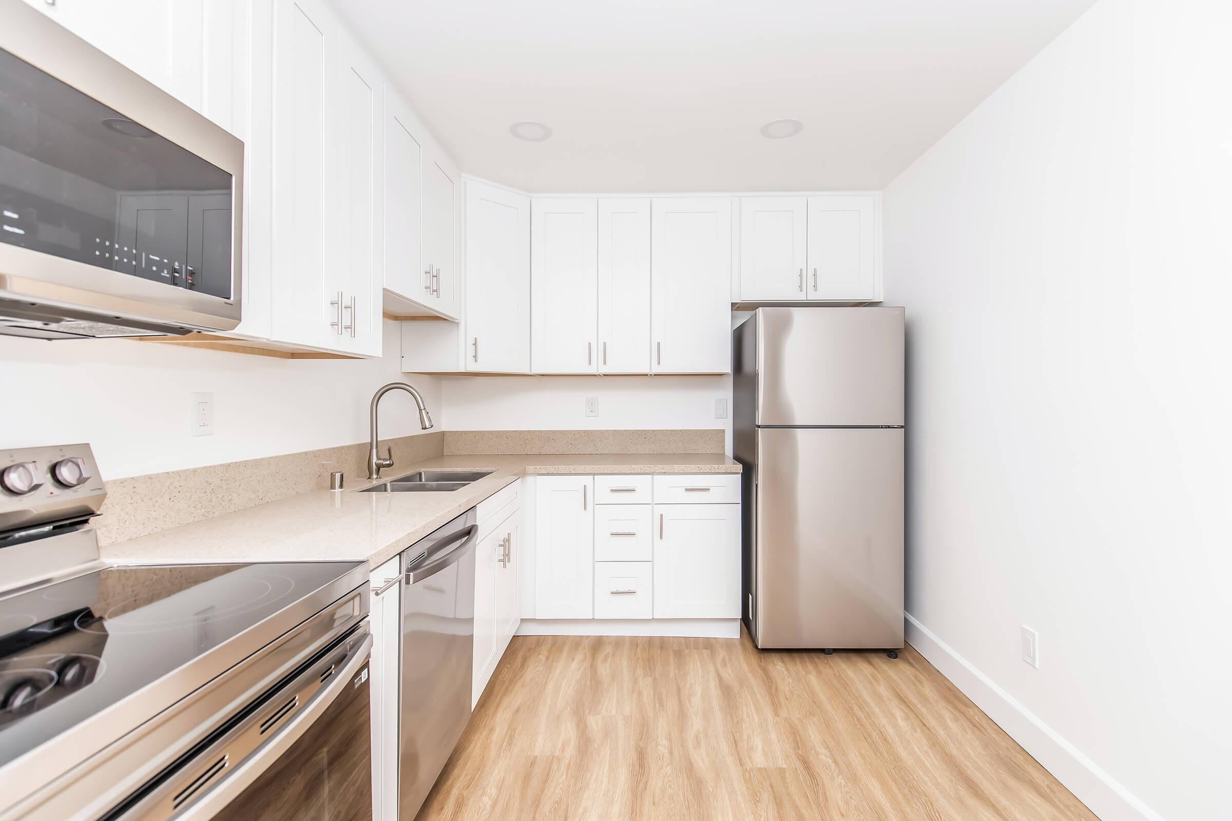 Modern kitchen featuring white cabinetry, stainless steel appliances including a refrigerator and oven, a clean countertop, and light-colored wood flooring. The space is bright and minimalistic, emphasizing functionality and style.