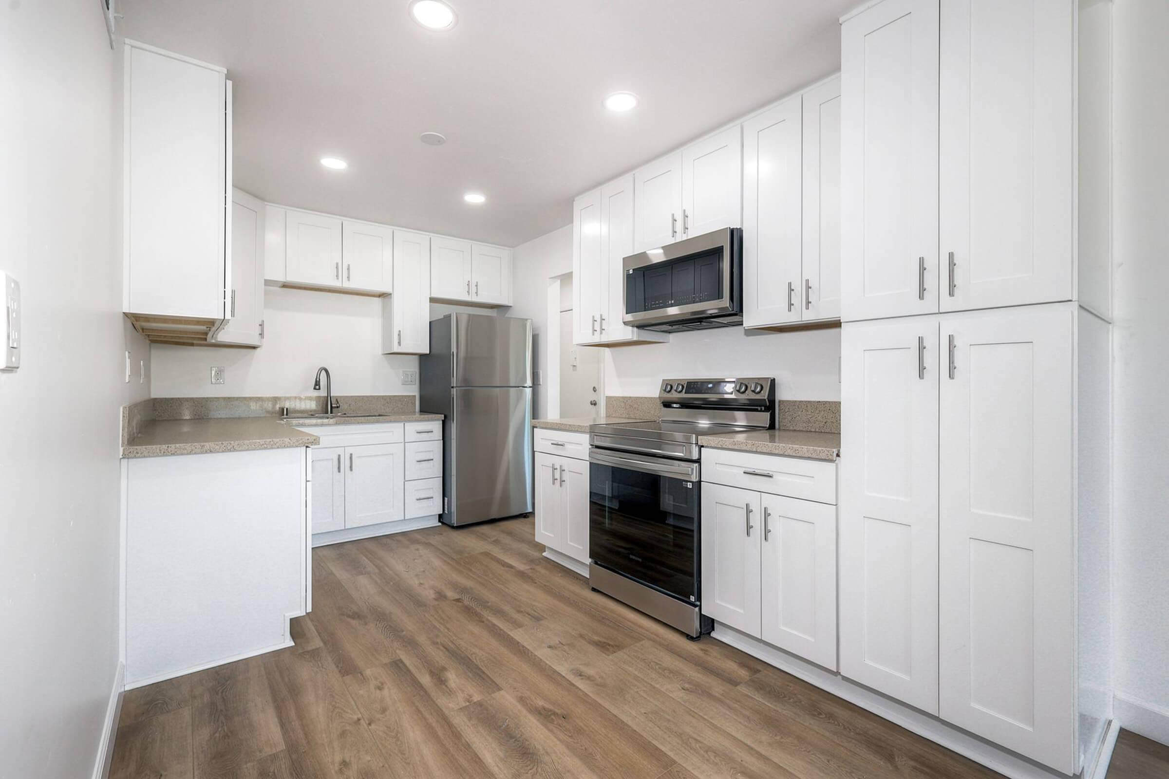 Modern kitchen featuring white cabinetry, granite countertops, stainless steel appliances, including a refrigerator, microwave, and oven. The space has a light and airy feel, with recessed lighting and wood-like flooring, offering a clean and contemporary design.