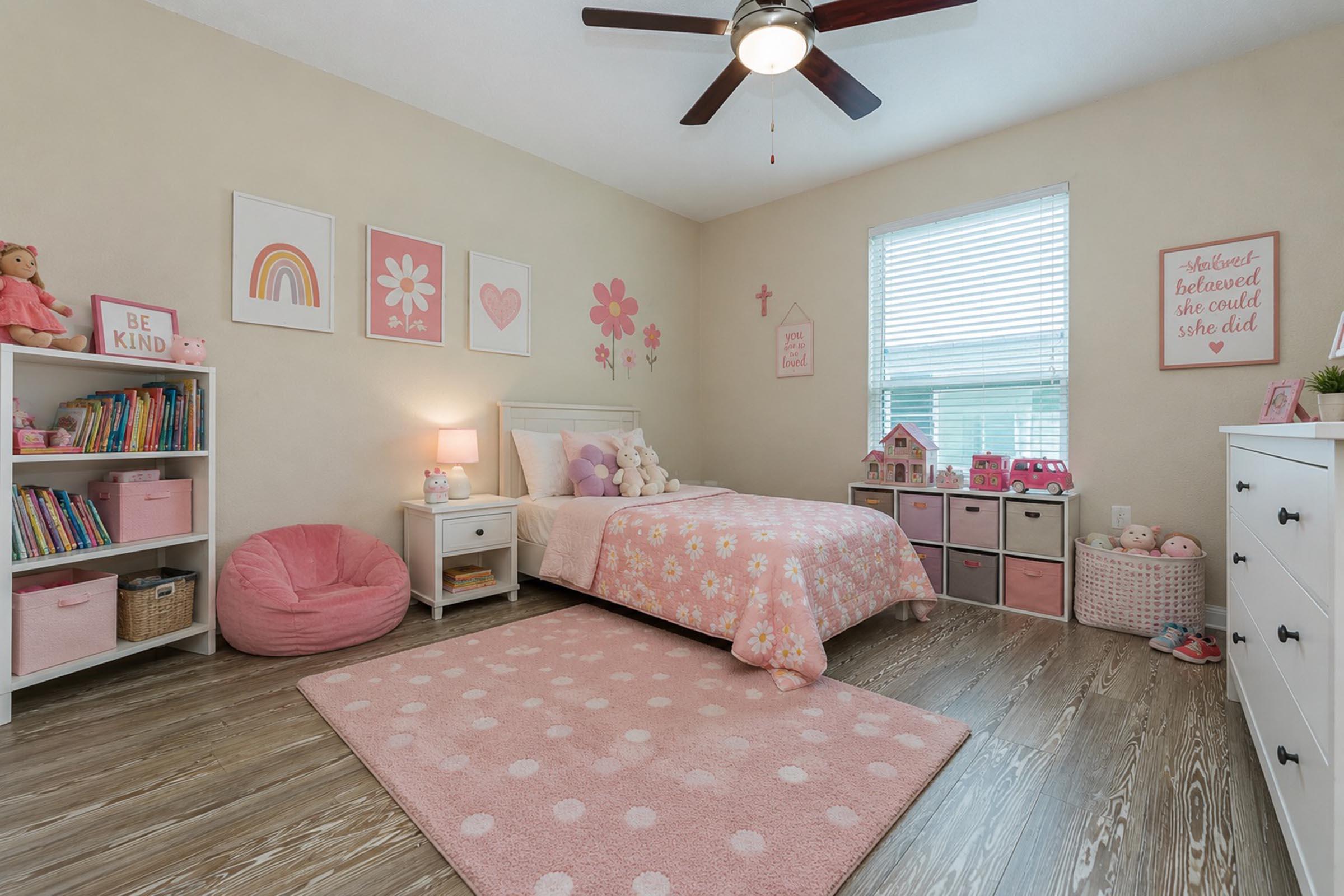 A cozy children's bedroom featuring a pink-themed decor. The room includes a white bed with flower-patterned bedding, a plush pink rug, a nightstand with a lamp, a bookshelf filled with books, storage bins, and wall art. A pink bean bag chair adds comfort, and there's a window with light curtains.