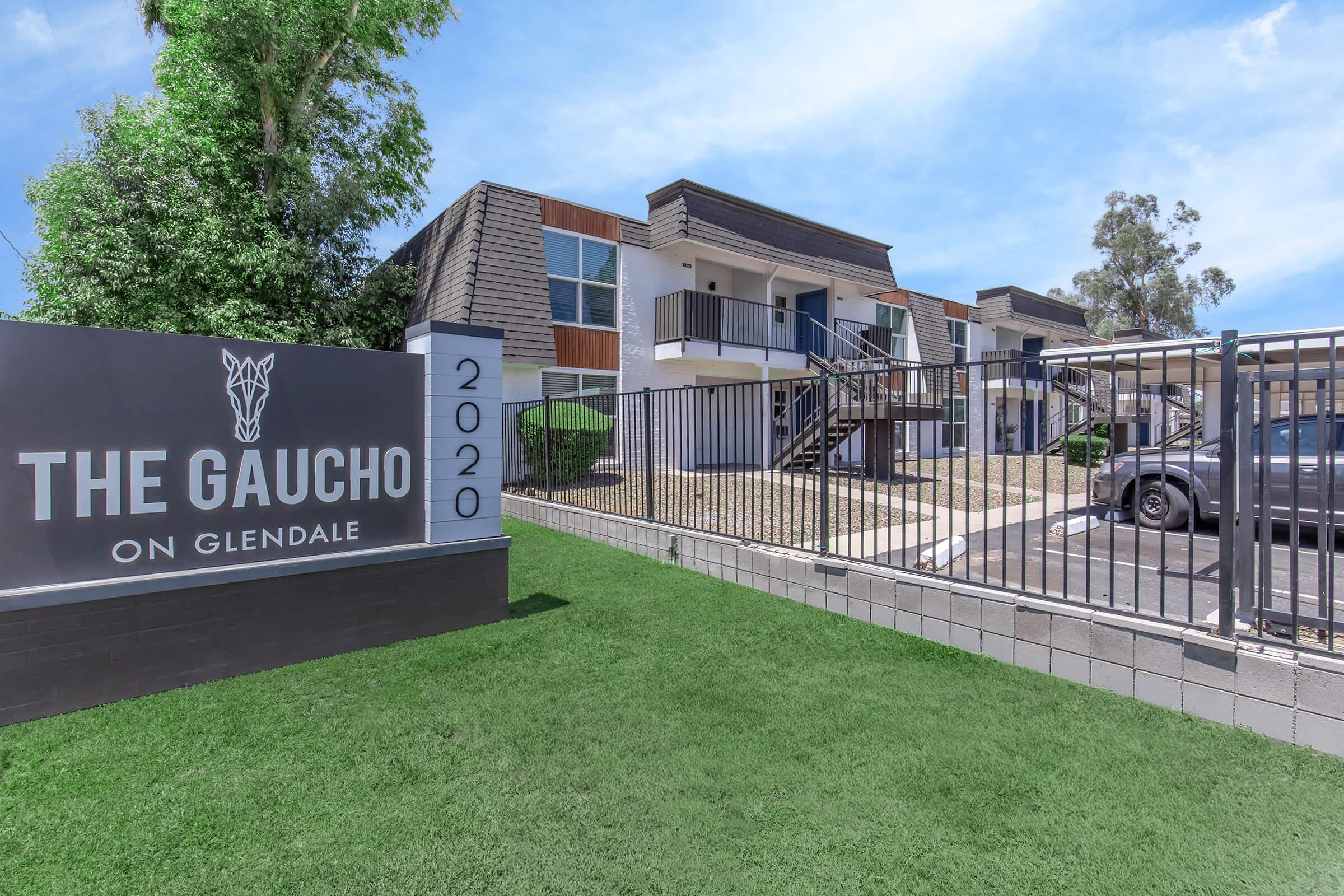 A modern apartment complex named "The Gaucho on Glendale," featuring a prominent sign with the year 2020. The property is set against a blue sky with greenery, highlighting a well-maintained exterior and parking area, enclosed by a fence.