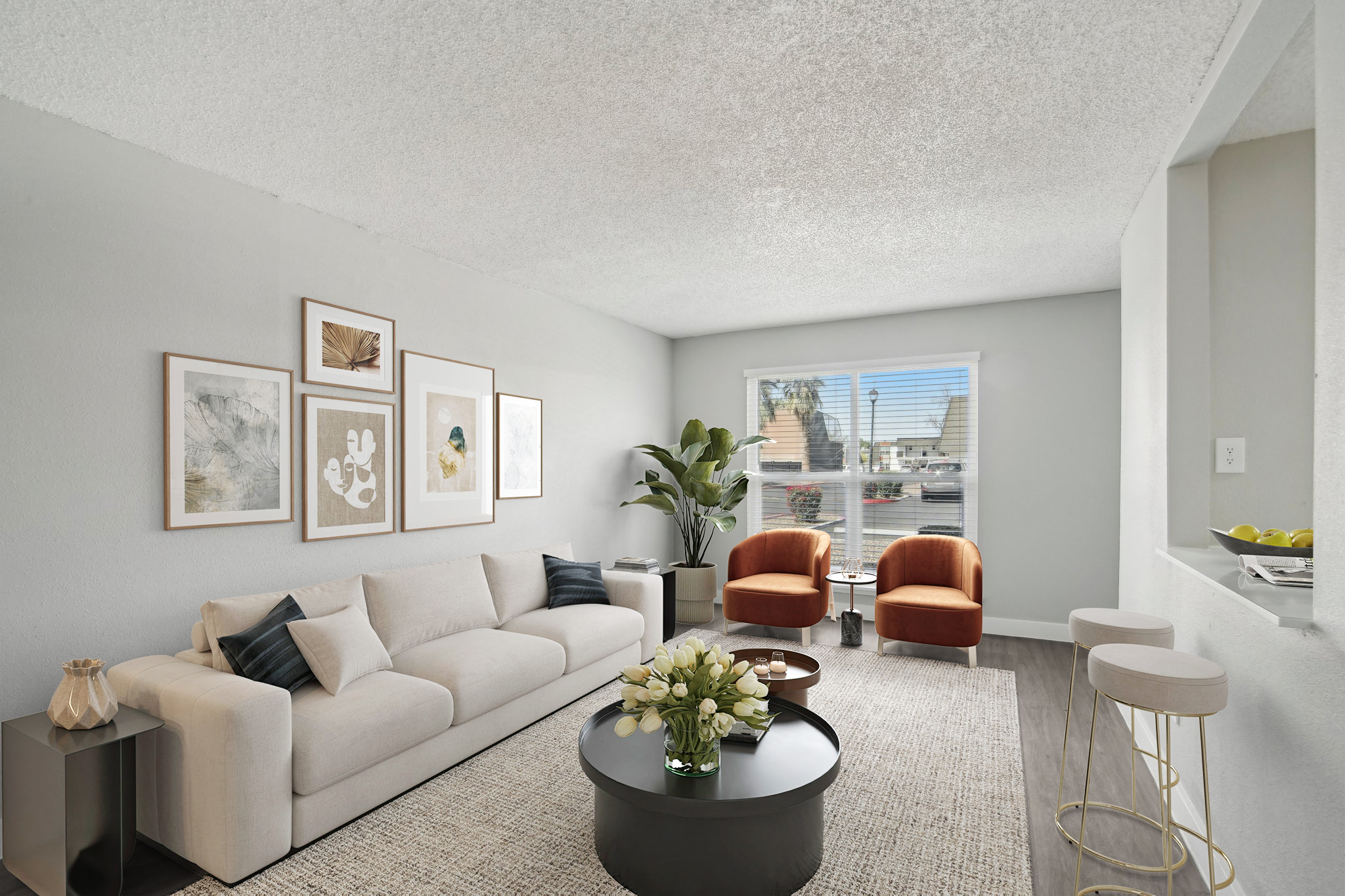 A modern living room featuring a light-colored sofa with decorative pillows, two orange accent chairs, a round black coffee table with flowers, and framed artwork on the walls. There is a large window with natural light and a green plant in the corner, creating a cozy and inviting atmosphere.