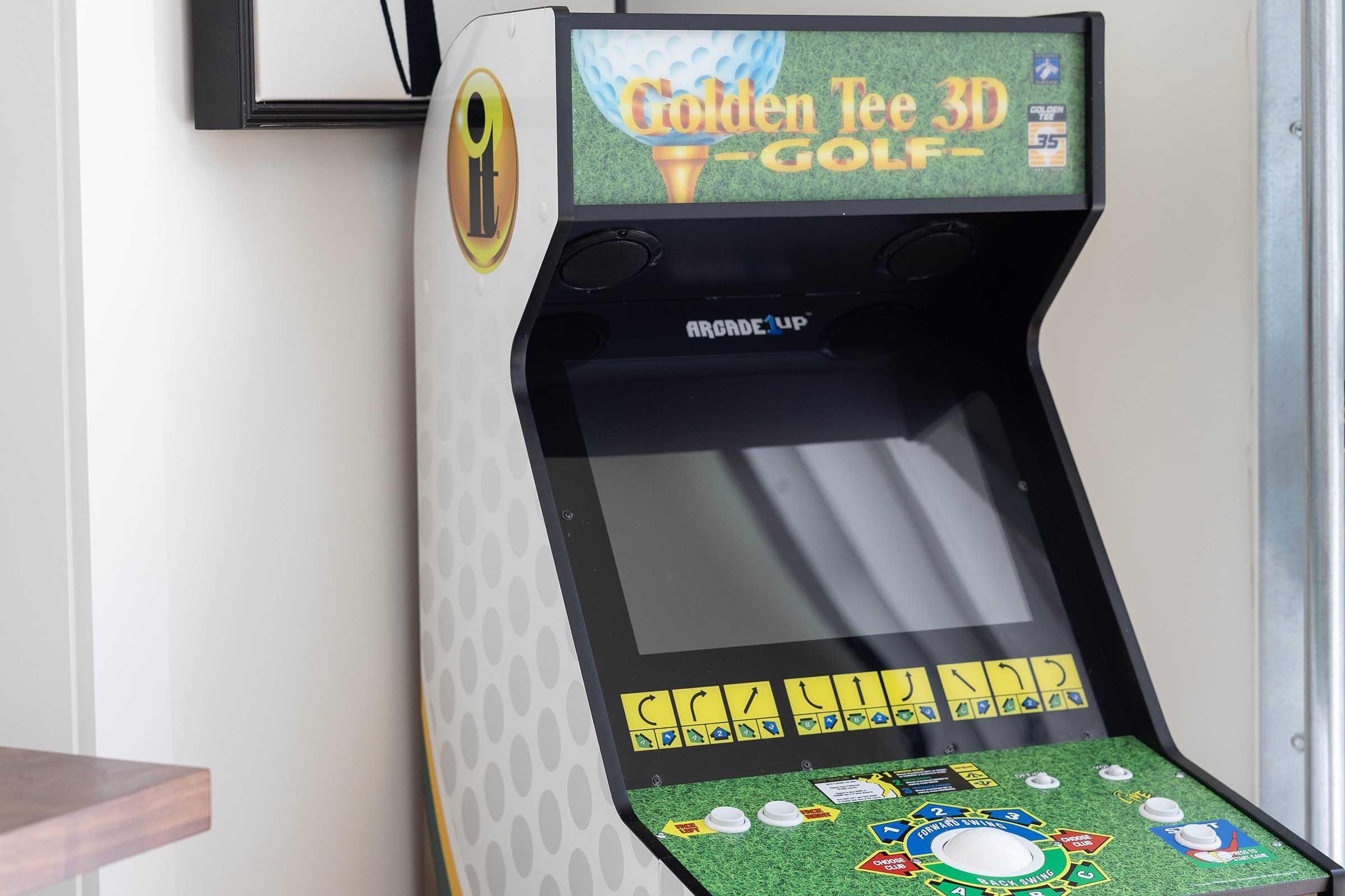 An arcade cabinet featuring the game "Golden Tee 3D Golf," showcasing a green turf design with a large screen and numerous control buttons. The cabinet is positioned against a wall, with a sleek and modern appearance.