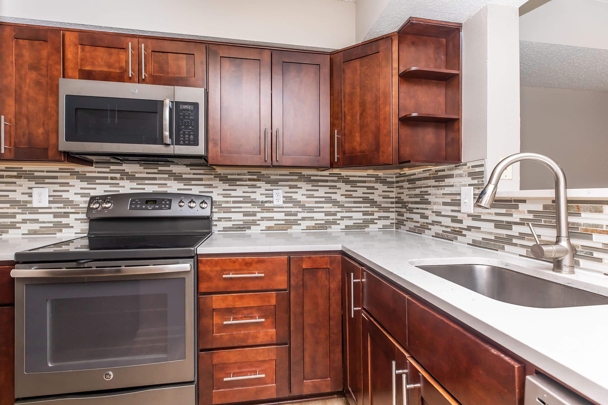 Modern kitchen featuring dark wood cabinetry, stainless steel appliances including a microwave and stove, and a sleek countertop with an undermount sink. The backsplash is decorated with a mix of light and dark tiles, creating a stylish contrast.