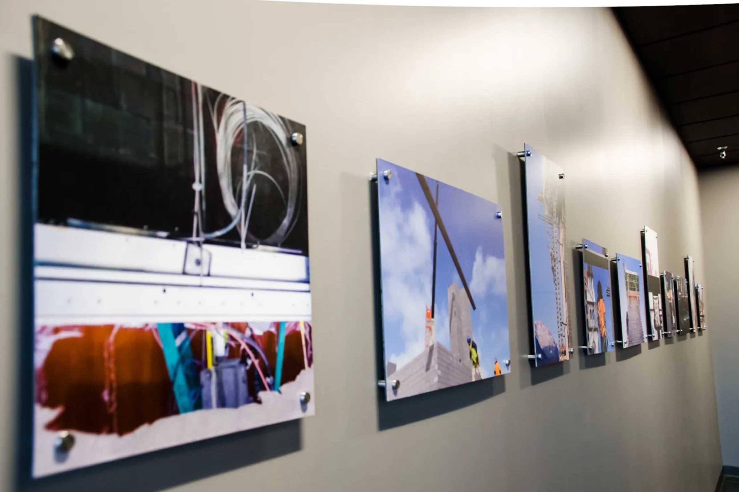 A series of photographs displayed on a wall, showcasing construction and architectural themes. The images depict various stages and elements of building, including tools, materials, and workers in action, all presented in a modern exhibition format with clear mounts.