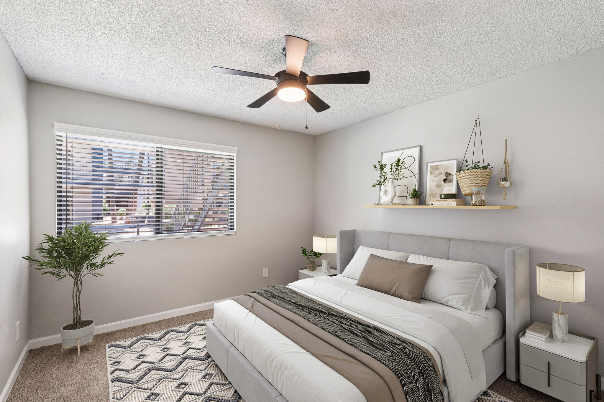 A modern bedroom with a light gray color scheme. It features a queen-sized bed with neutral bedding and a decorative throw. A ceiling fan hangs above, and there are two bedside lamps on matching nightstands. A window with blinds allows natural light in, and potted plants add greenery to the space.