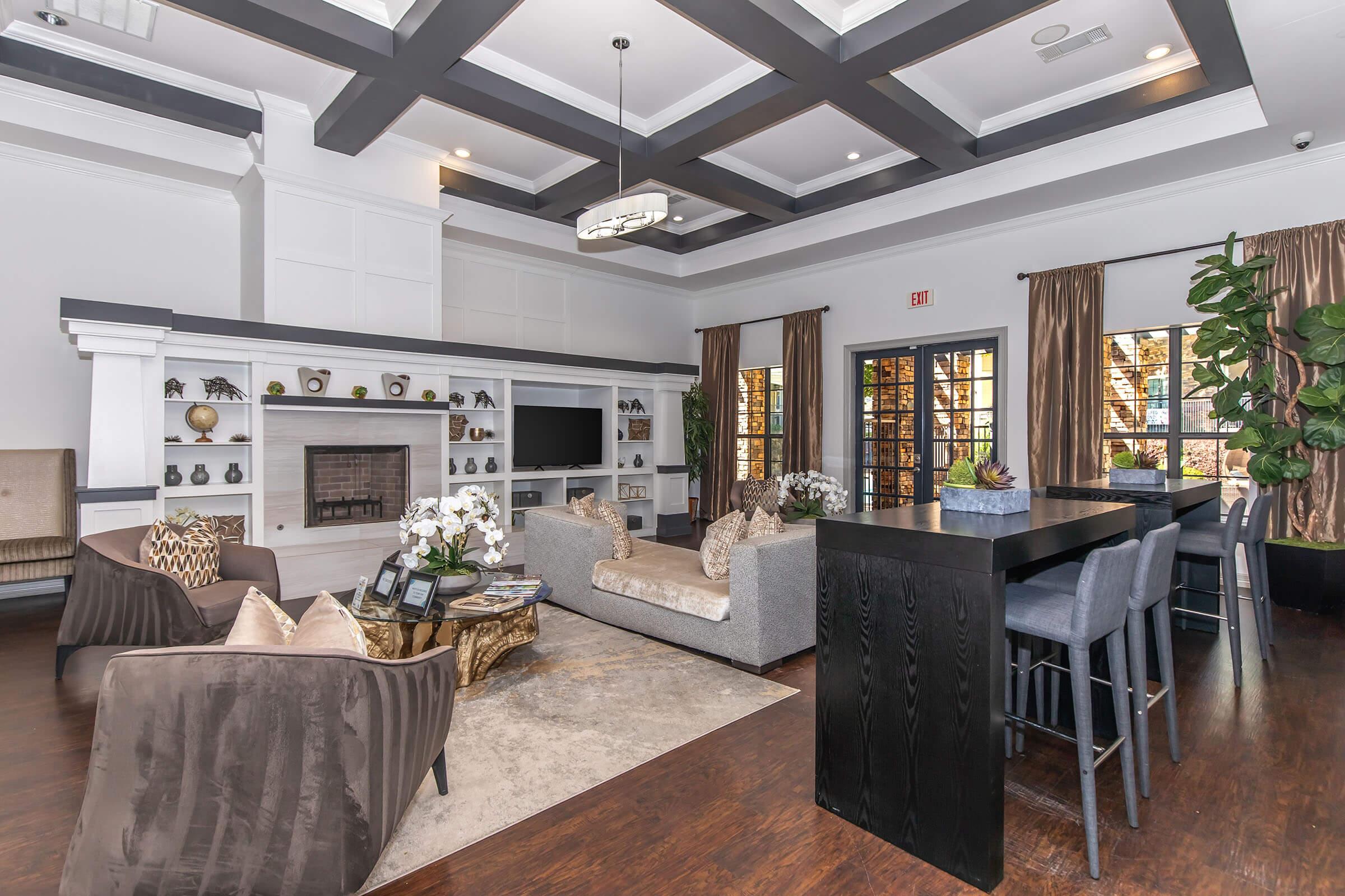 A stylish lounge area featuring comfortable seating, a modern fireplace, and large windows with elegant curtains. The space is decorated with decorative plants and a coffee table, creating an inviting atmosphere for relaxation or socializing. The color scheme combines neutral tones with a touch of elegance.