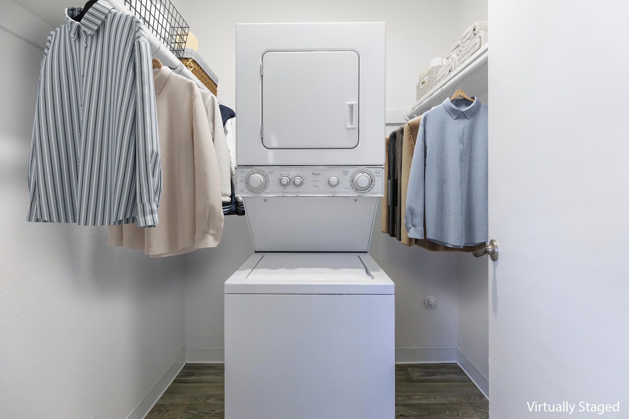 A compact laundry area featuring a stacked washer and dryer unit in a closet. On either side, neatly hung clothes including striped and solid-colored shirts. The space is well-lit and organized, showcasing a tidy and functional laundry setup.