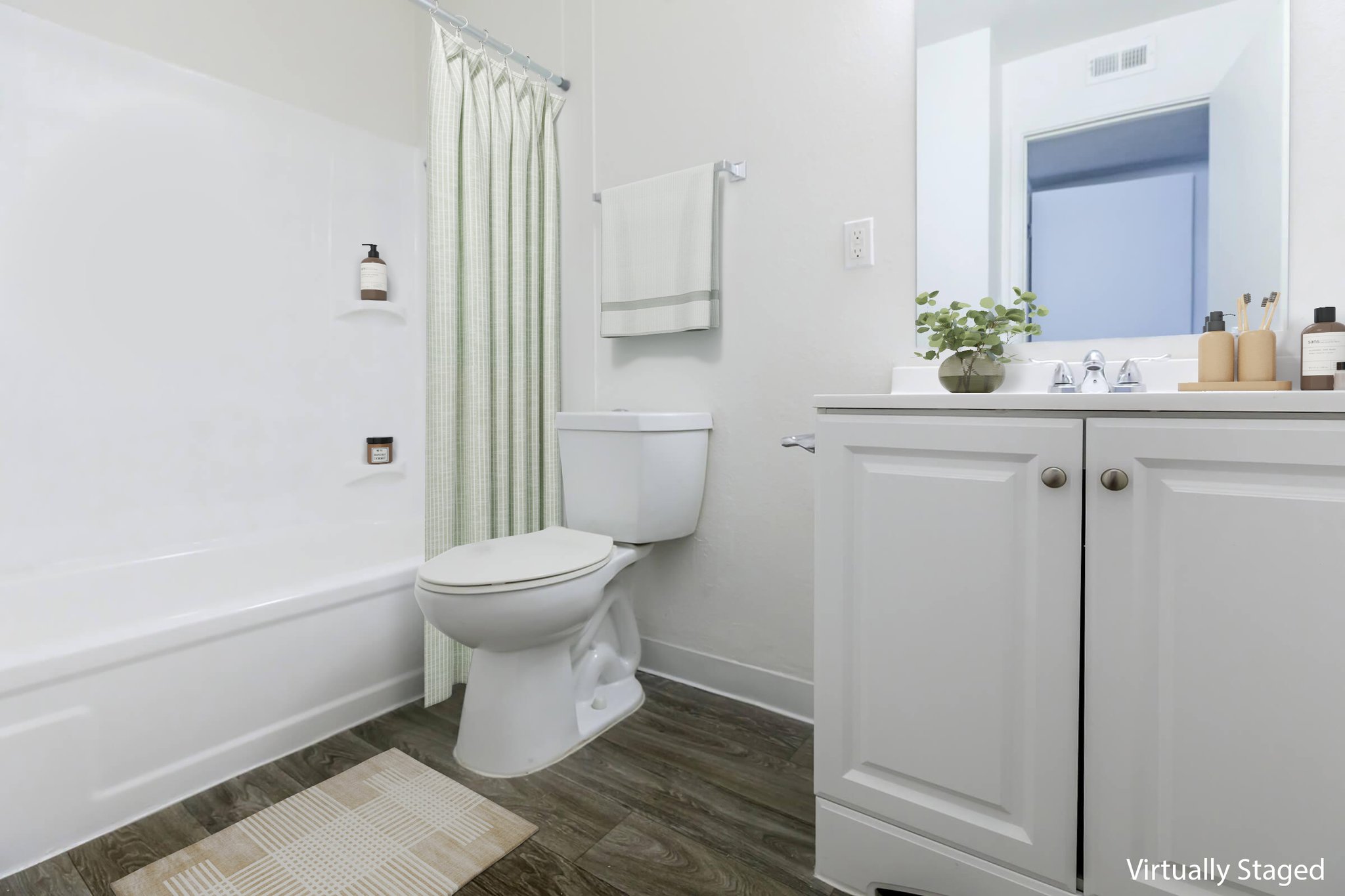 Modern bathroom featuring a white bathtub with a shower curtain, a clean toilet, and a stylish vanity with a sink. There is a small plant on the counter, and toiletries are neatly arranged. The walls are light-colored, and the flooring has a wood-like appearance, creating a bright and inviting atmosphere.