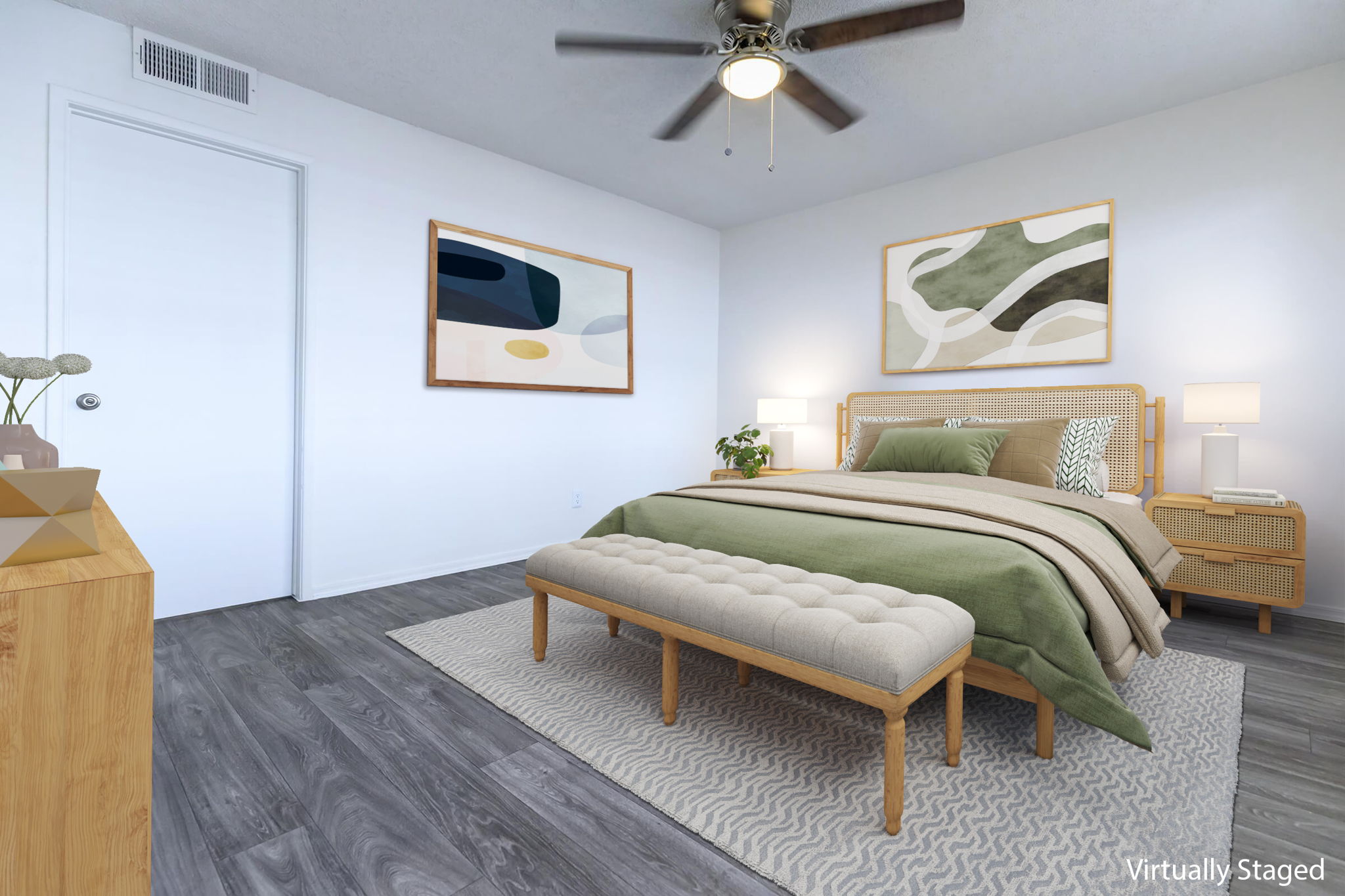 A modern, virtually staged bedroom featuring a wooden bed with green and beige bedding, a matching bench at the foot, two bedside tables with lamps, and abstract wall art. The flooring is dark, and there is a ceiling fan. A white door leads to another room, enhancing the bright and inviting atmosphere.