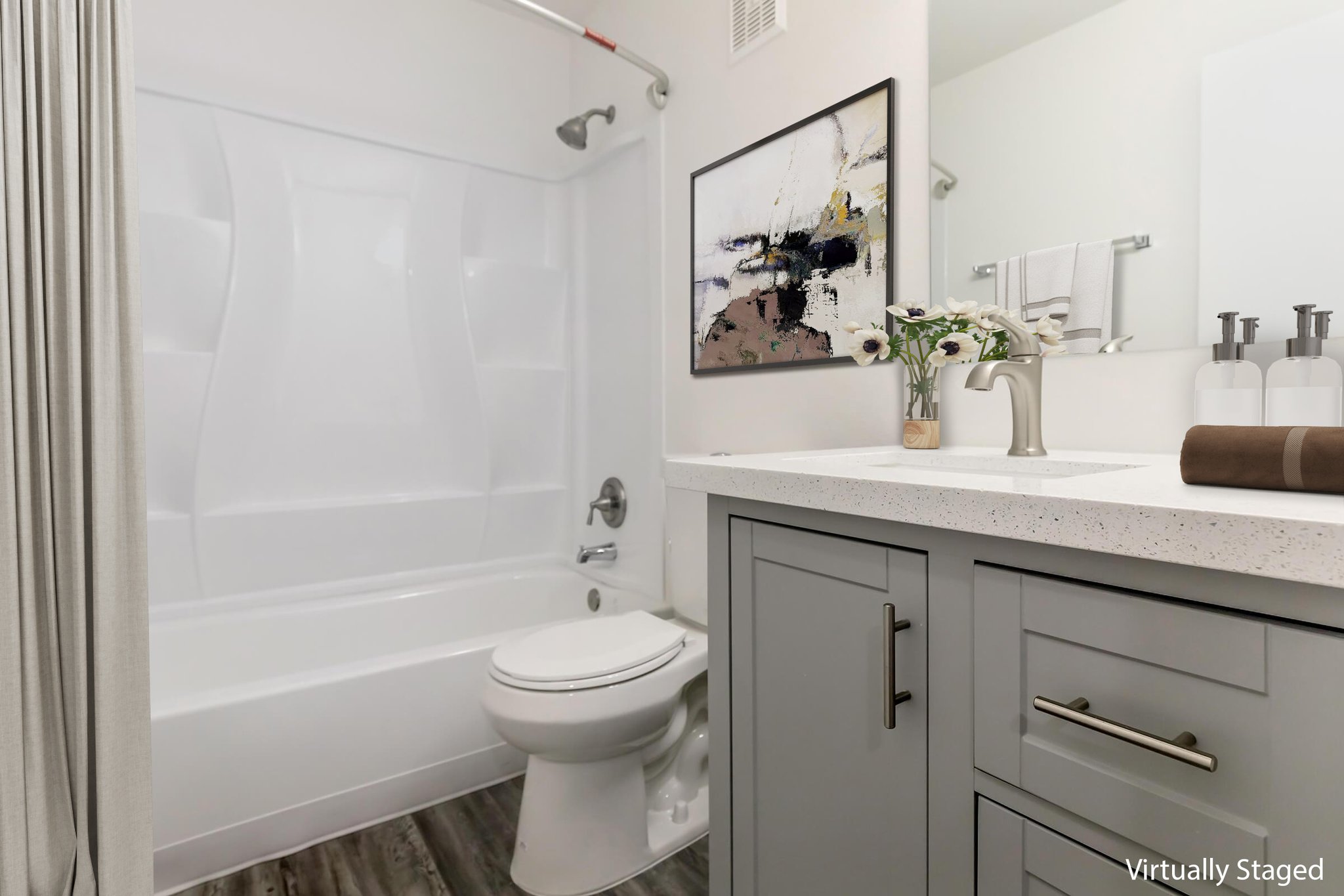 Modern bathroom featuring a white bathtub and shower combination, a sleek vanity with gray cabinetry, a stylish sink faucet, and decorative elements including a small vase of flowers and framed artwork on the wall. Soft lighting enhances the space's inviting atmosphere.