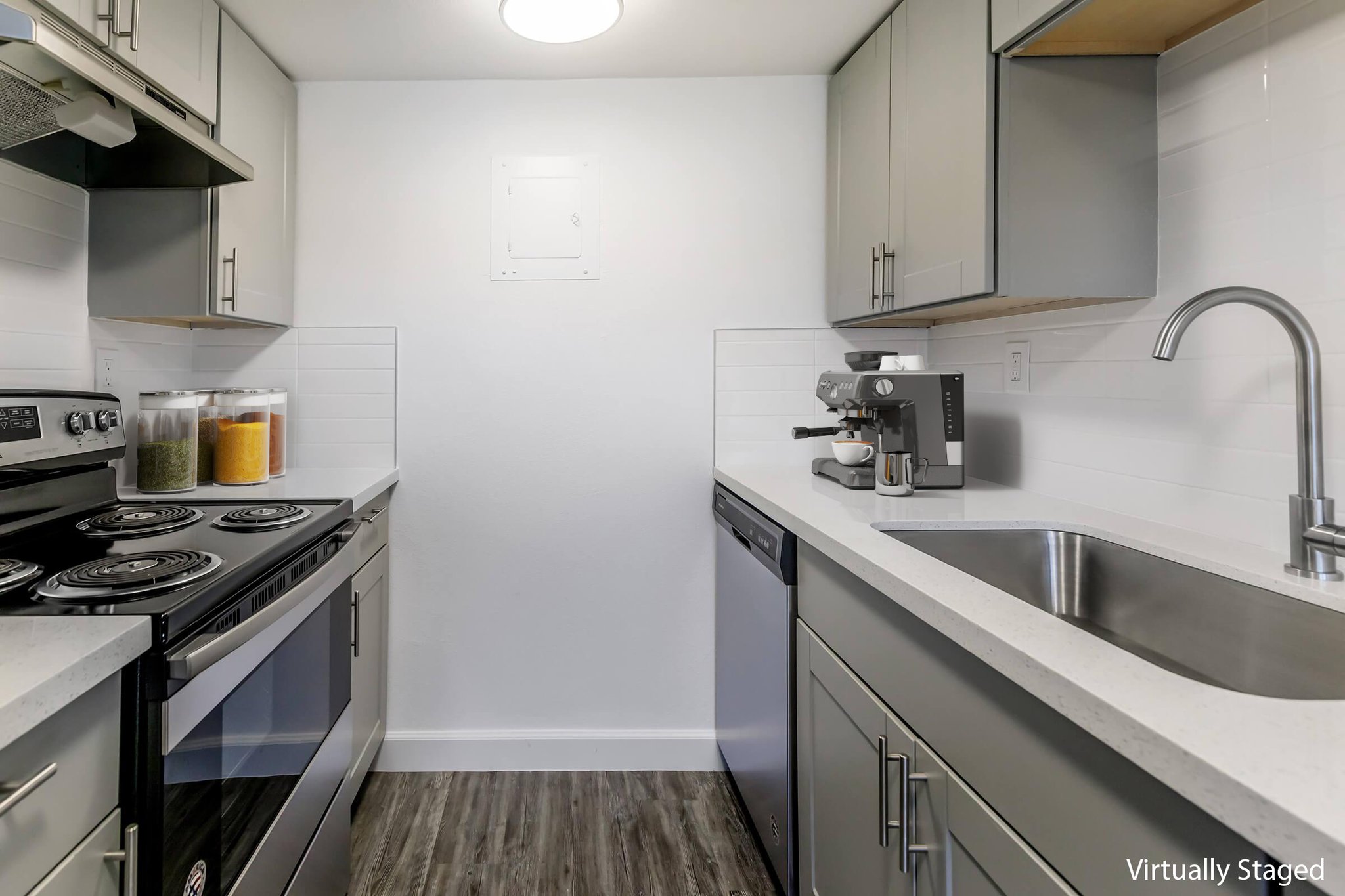 A modern kitchen featuring stainless steel appliances, including a stove, oven, and dishwasher. The countertops are white with a sleek design, and there's a coffee maker on the counter. Clear containers with various ingredients are stored on the shelf, and the walls are painted a light color for a bright atmosphere.