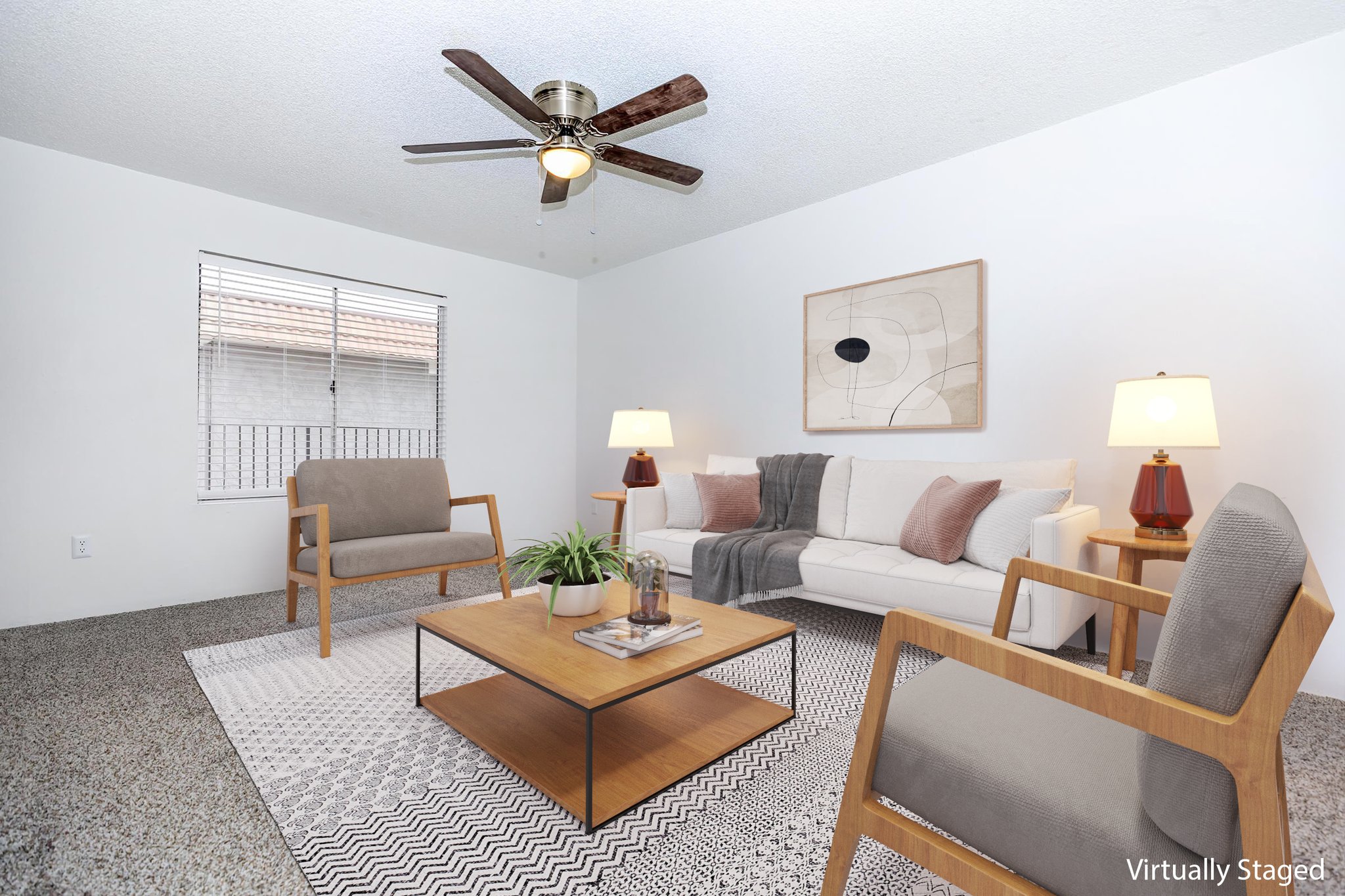 A bright and inviting living room featuring a light-colored sofa with decorative pillows, two stylish armchairs, a coffee table, and a geometric area rug. The space includes a ceiling fan and two lamps for warm lighting, with a decorative artwork on the wall and a window allowing natural light to flow in.