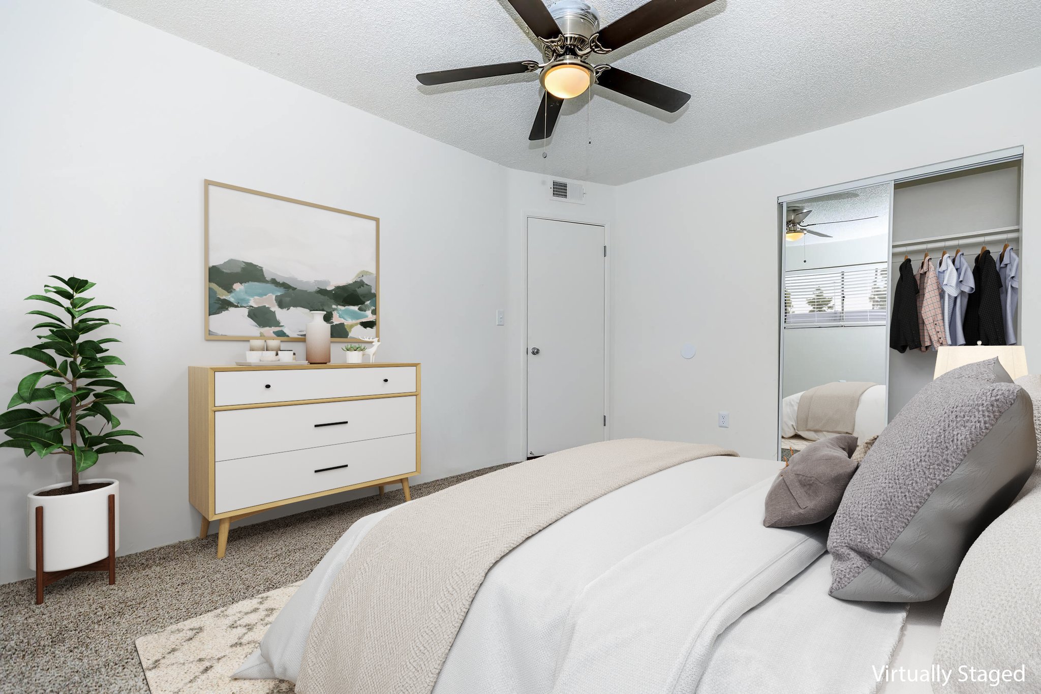 A cozy bedroom featuring a neatly made bed with decorative pillows, a stylish dresser, a potted plant, and a ceiling fan. The room is painted in neutral tones, with large windows allowing natural light and visible closet space in the background.