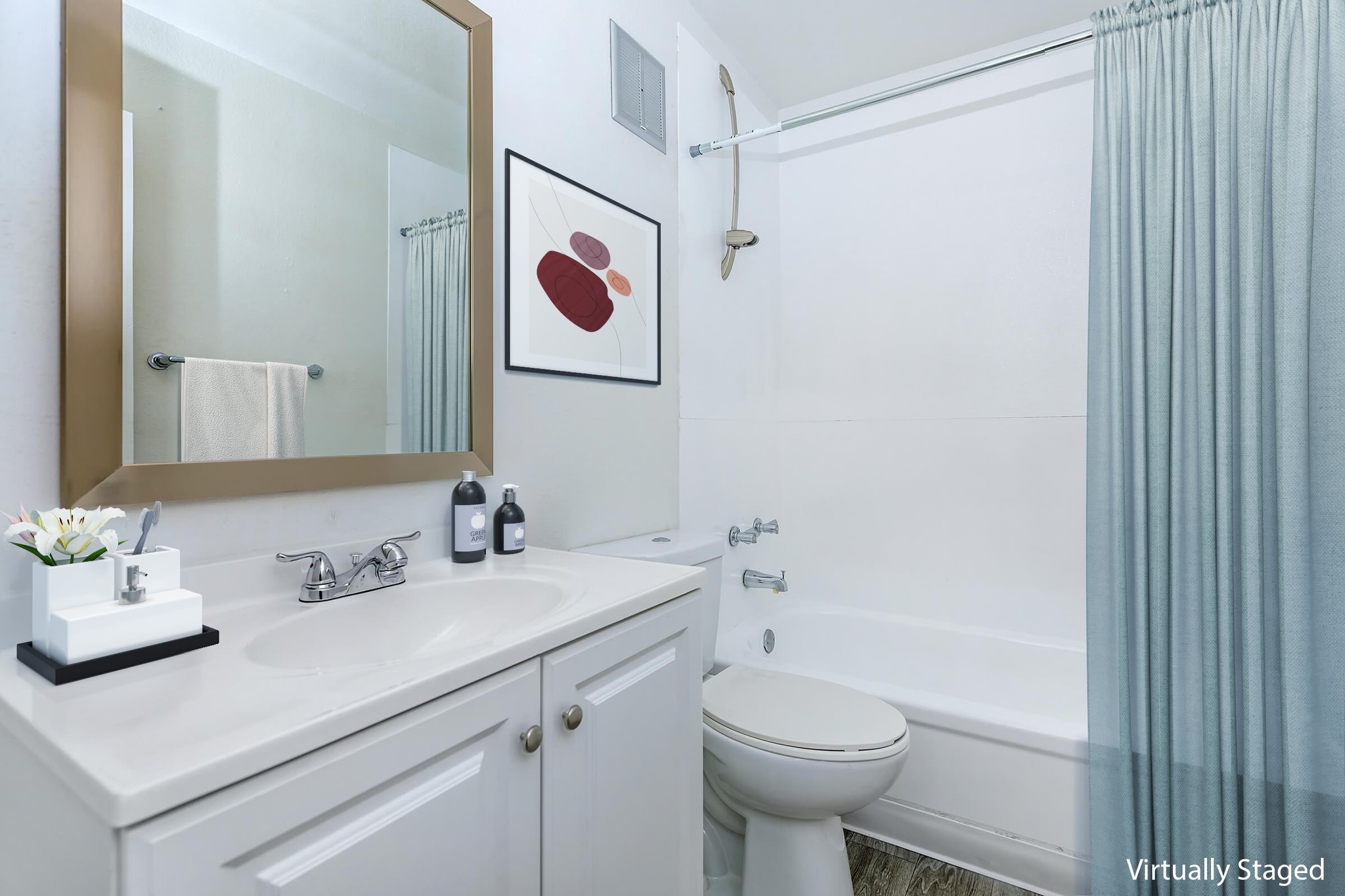 A modern bathroom featuring a white vanity with a sink, a round mirror, and neatly arranged toiletries. The space includes a white bathtub with a shower curtain in a light blue color, a decorative wall art above the vanity, and a towel hanging on the wall. Natural light brightens the area.