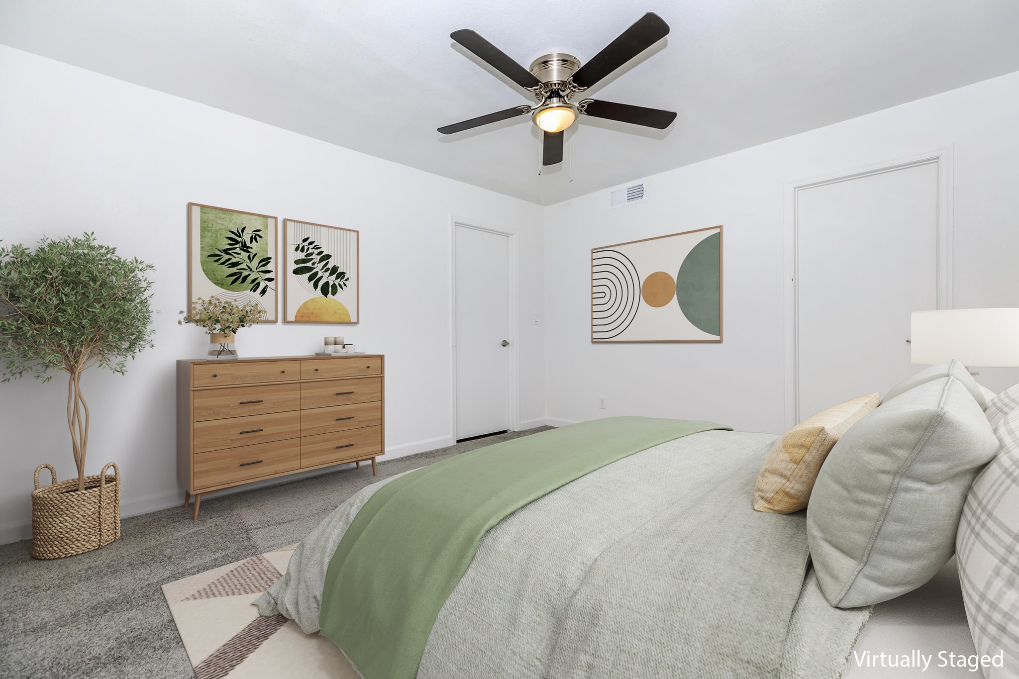 A modern bedroom featuring a bed with green and neutral bedding, a wooden dresser, and two framed artwork pieces on the walls. A potted plant adds green accents, and the room has a ceiling fan and light. The overall decor is stylish and minimalist, creating a serene atmosphere.