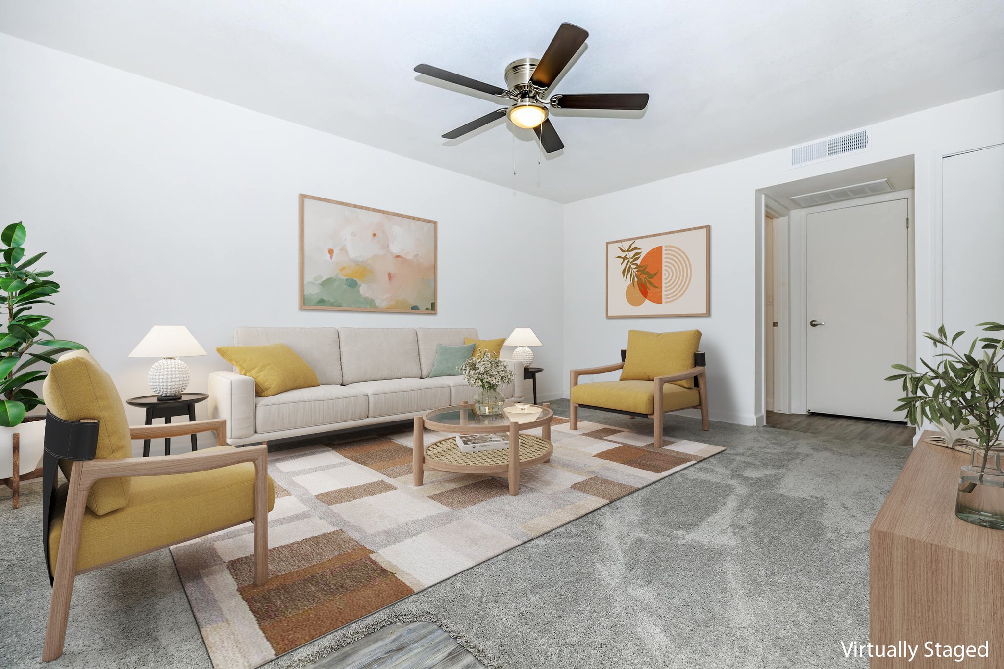 A modern living room featuring a light-colored sofa with decorative cushions, two yellow accent chairs, and a round coffee table on a patterned rug. There are indoor plants, a ceiling fan, and abstract art on the walls, creating a bright and inviting atmosphere.