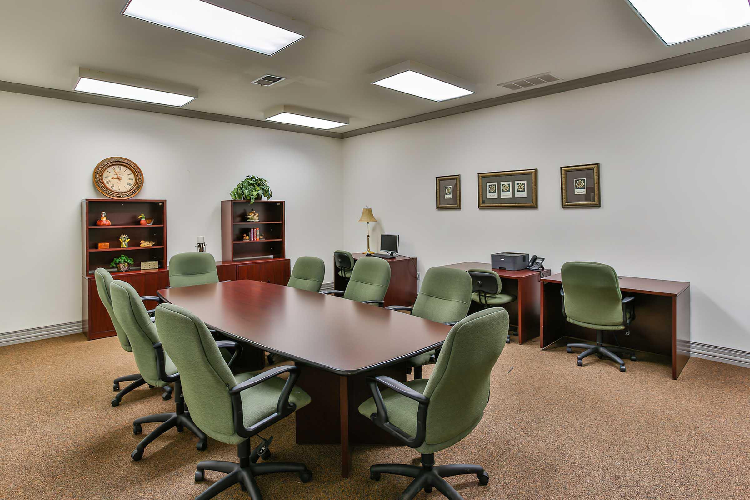 A modern conference room featuring a long rectangular table surrounded by green chairs.