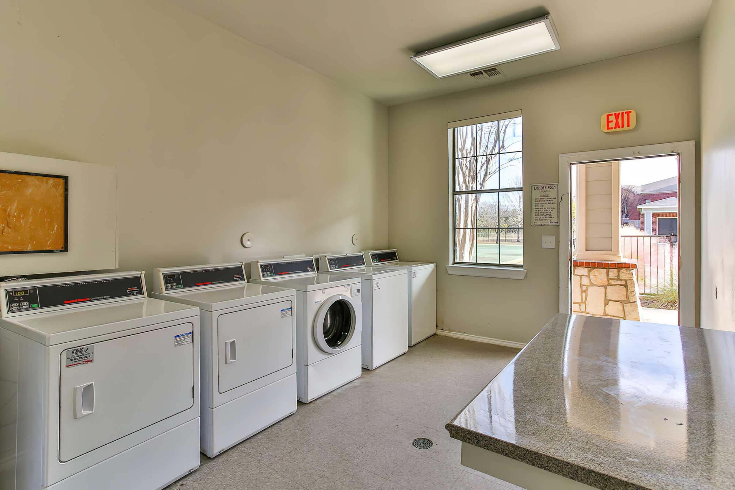 A clean laundry room featuring several white washing machines and a dryer lined up against the wall.