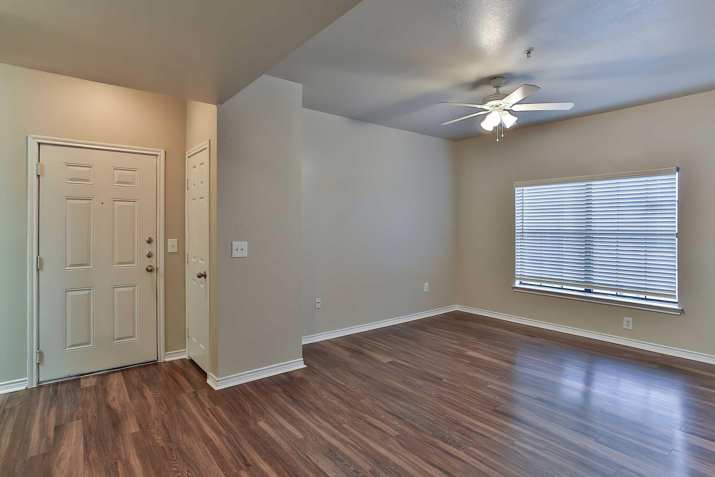 An empty living room with light brown walls and hardwood flooring.