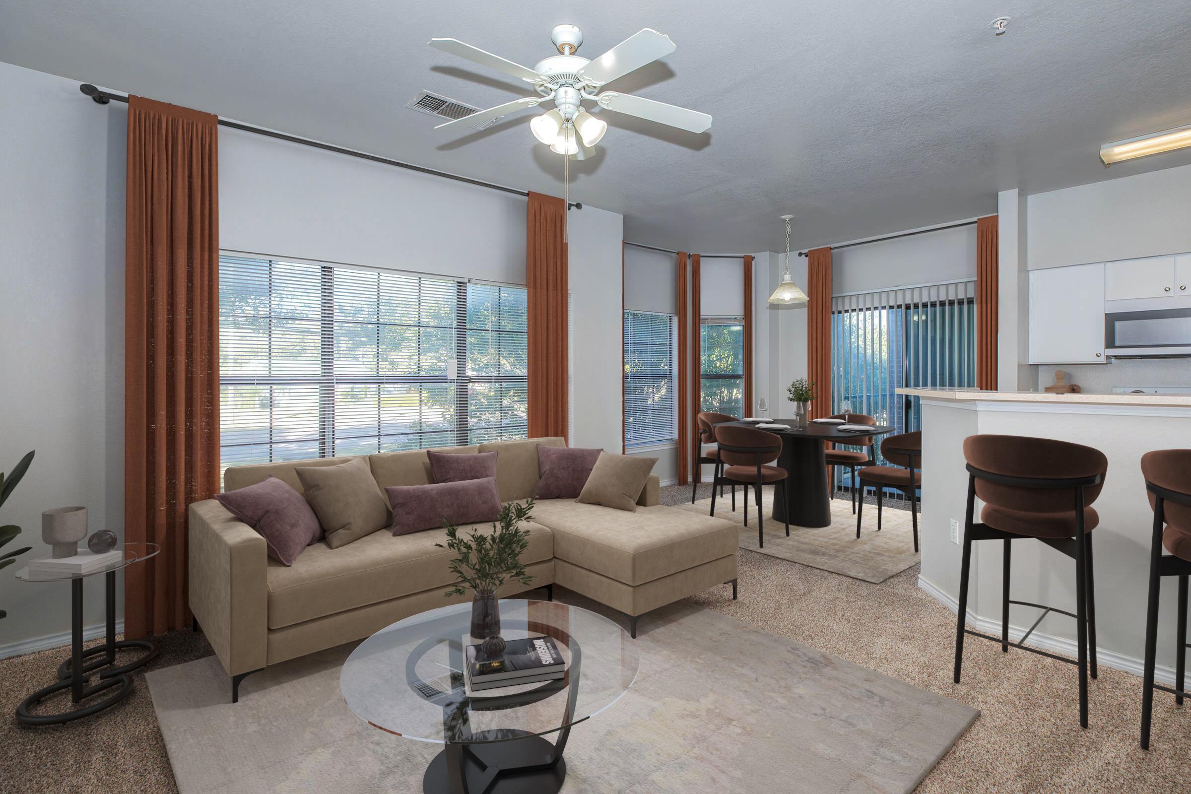 A cozy living room featuring a light-colored sectional sofa with purple pillows, a glass coffee table, and large windows with natural light. There is a dining area with a round table and chairs, along with a kitchen bar with stools. The decor includes warm curtains and a tasteful rug.