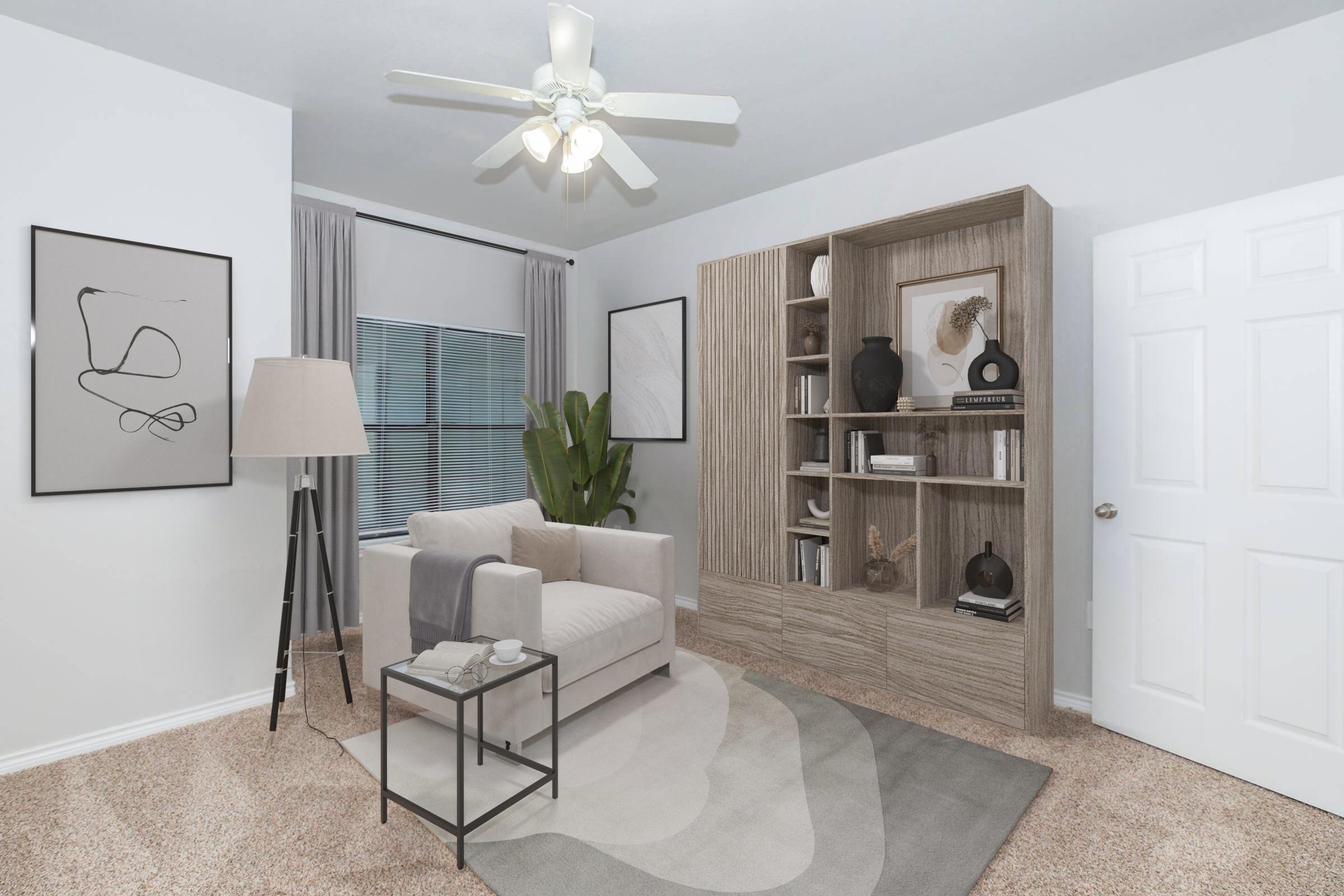 A cozy room featuring a light-colored sofa, a small black coffee table, and a modern floor lamp. A tall bookshelf filled with decorative items stands against the wall, complemented by a large indoor plant. The room has soft lighting from a ceiling fan and neutral artwork on the walls, creating a welcoming atmosphere.