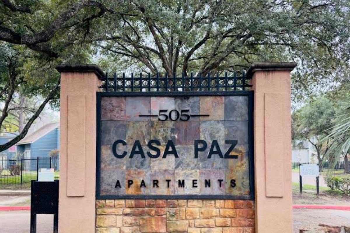 Sign for Casa Paz Apartments located at 505, featuring a natural stone design and surrounded by trees. The sign prominently displays the name "CASA PAZ" in bold letters, with "APARTMENTS" below it.