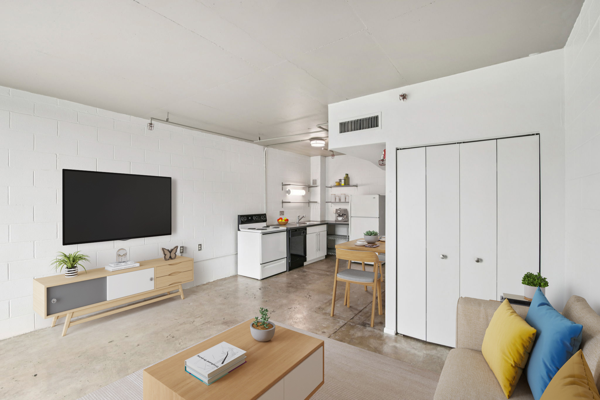 A modern living space with a light color palette. It features a comfortable sofa with colorful pillows, a coffee table, and a flat-screen TV mounted on the wall. The open kitchen includes a stove and a fridge, while a dining table with chairs is positioned nearby. The floors are concrete, providing a contemporary look.