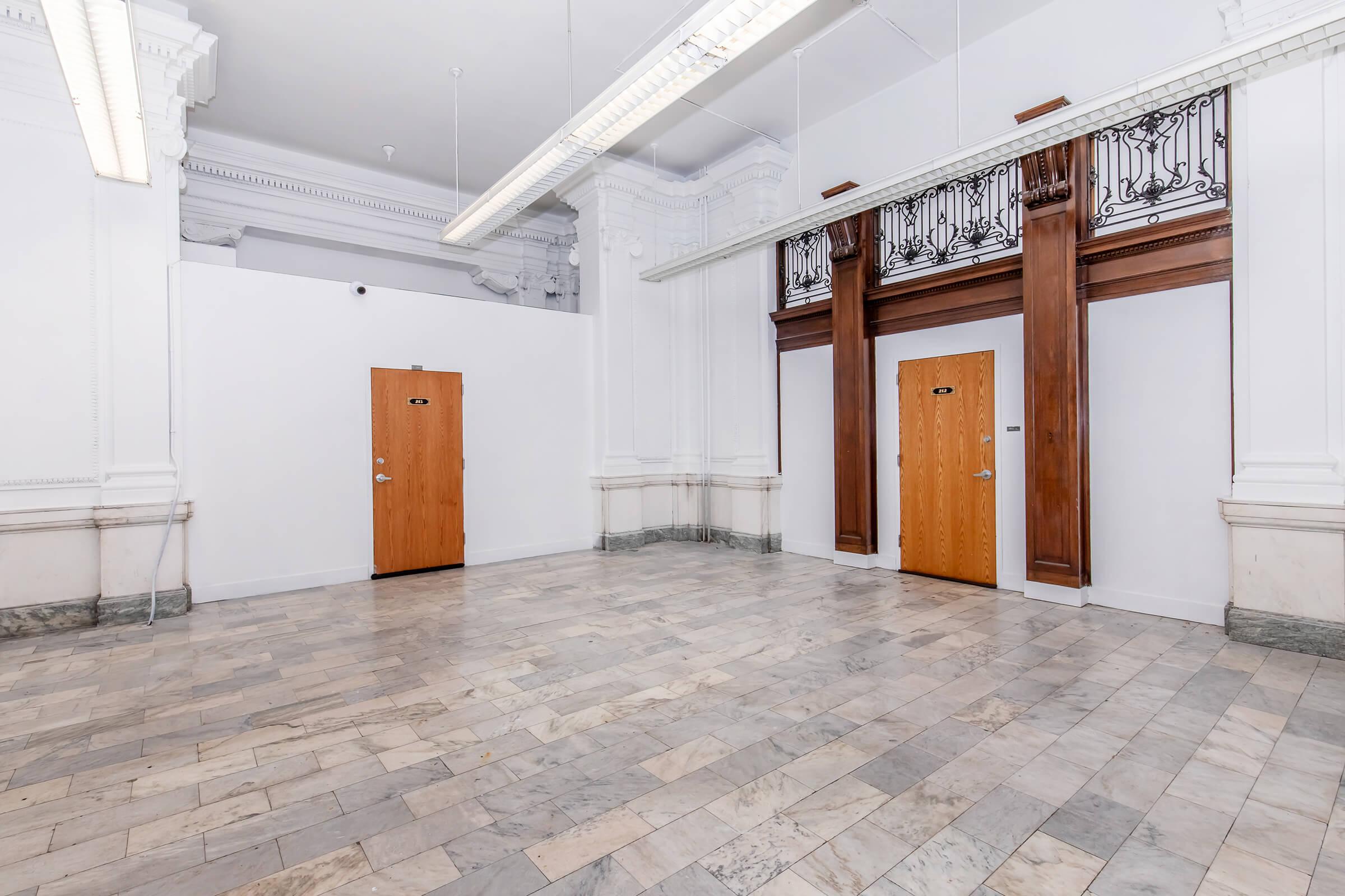 Empty interior space featuring marble flooring, two closed wooden doors with signs, and decorative architectural details on the walls and ceiling.