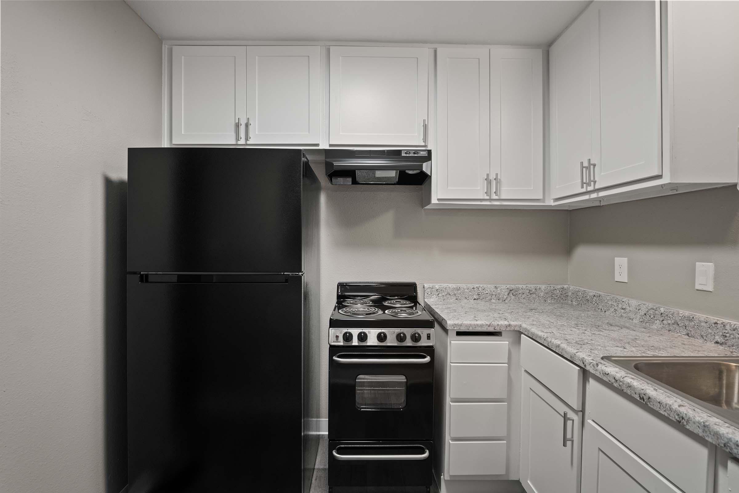 Modern kitchen featuring white cabinetry, a black refrigerator, stainless steel oven and cooktop, and a granite countertop. The design is clean and functional, with a sink and ample storage space. The walls are painted in a neutral color, enhancing the spacious feel.