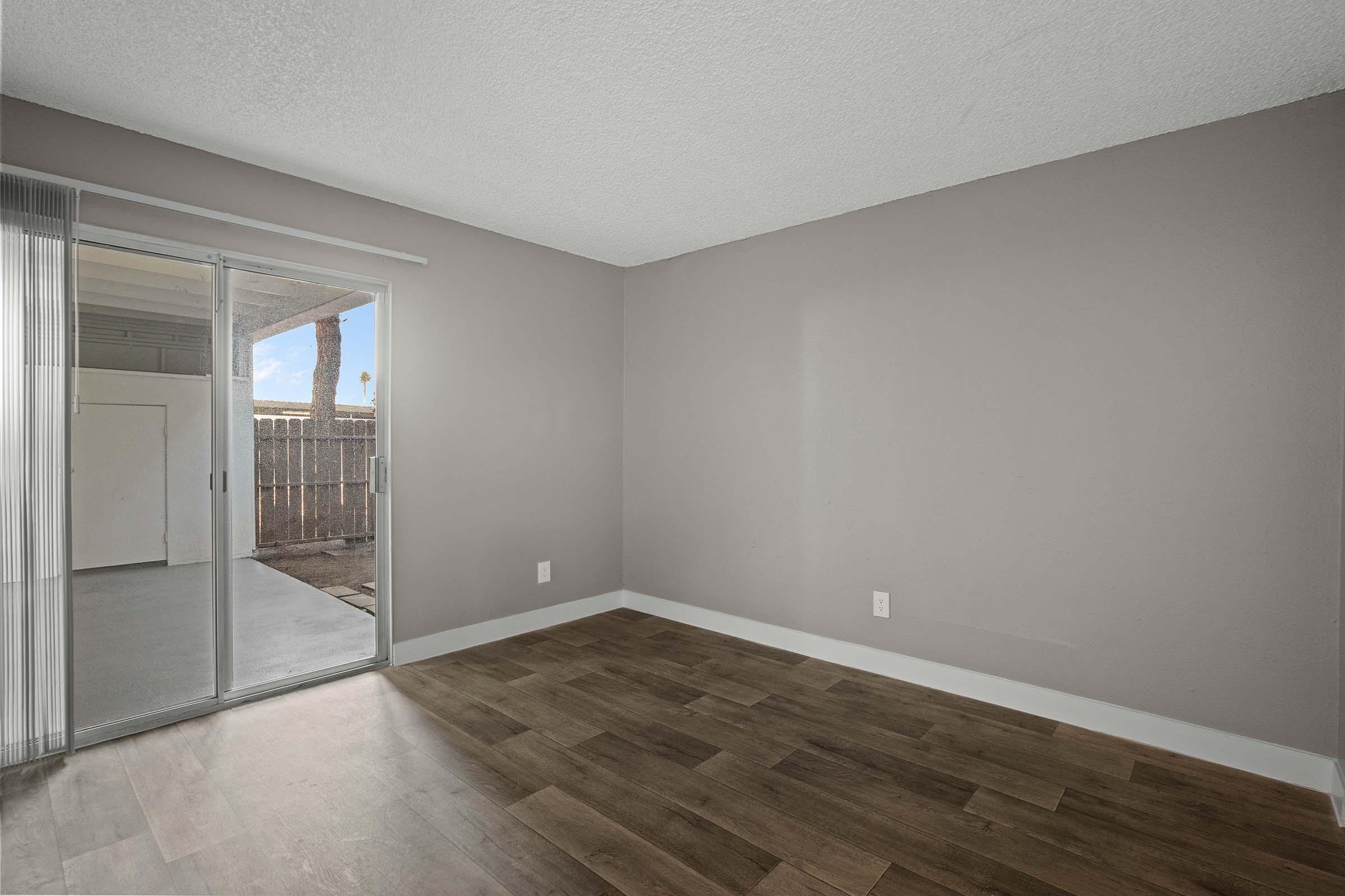 Interior view of a empty room with light purple walls and wooden flooring. A sliding glass door leads to an outdoor area, providing natural light. The space appears spacious and unfurnished, ideal for personal decoration and use.
