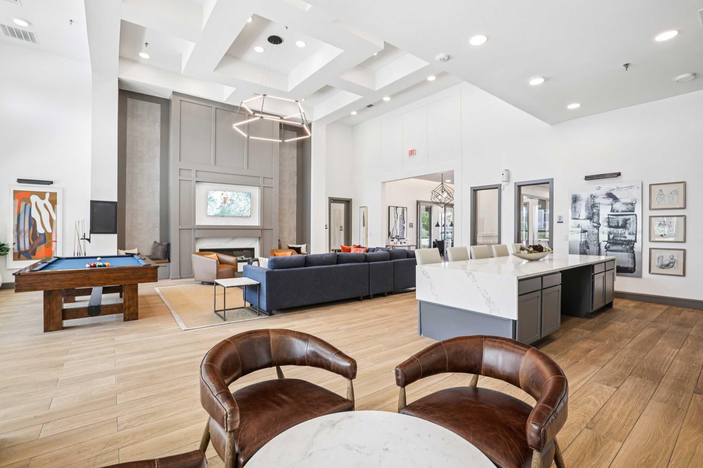 Modern interior of a spacious lounge area featuring a large seating arrangement, flat-screen TV, and a dining space. There’s a billiards table and contemporary artwork on the walls, with wooden flooring and stylish lighting fixtures enhancing the ambiance.