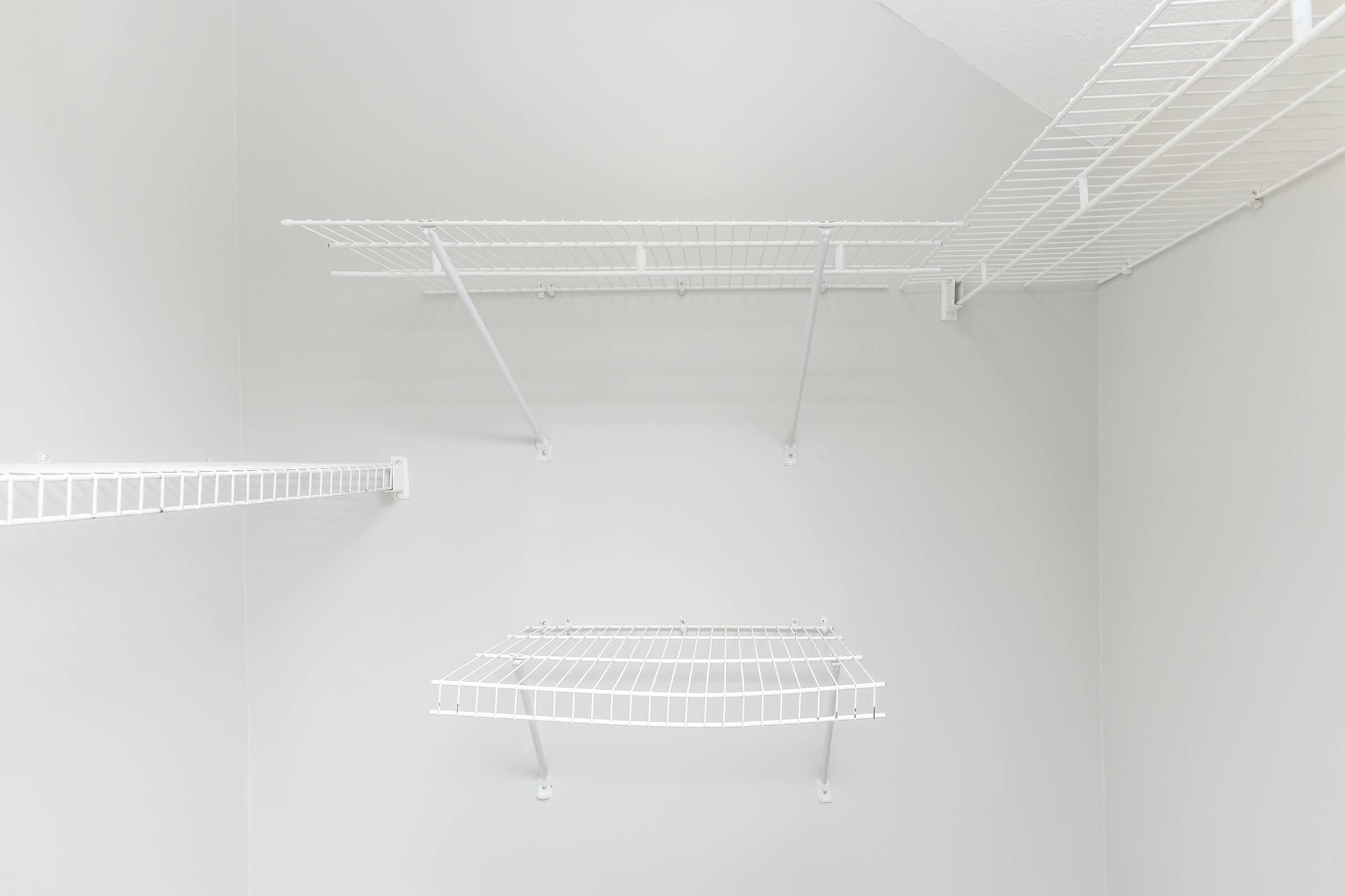 Empty closet with white wire shelving installed on light gray walls. The shelves are arranged in a minimalist style, providing open storage space.