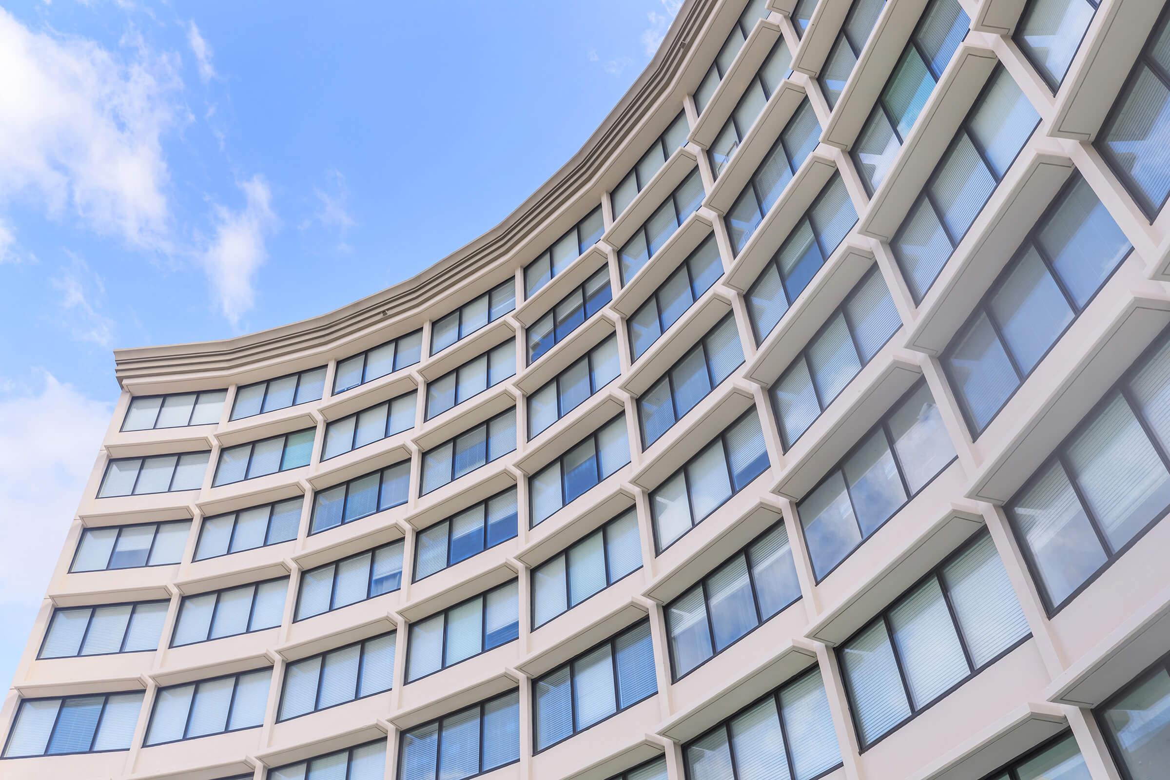 A modern building with a curved exterior featuring multiple rows of large windows against a clear blue sky, showcasing architectural design and symmetry.