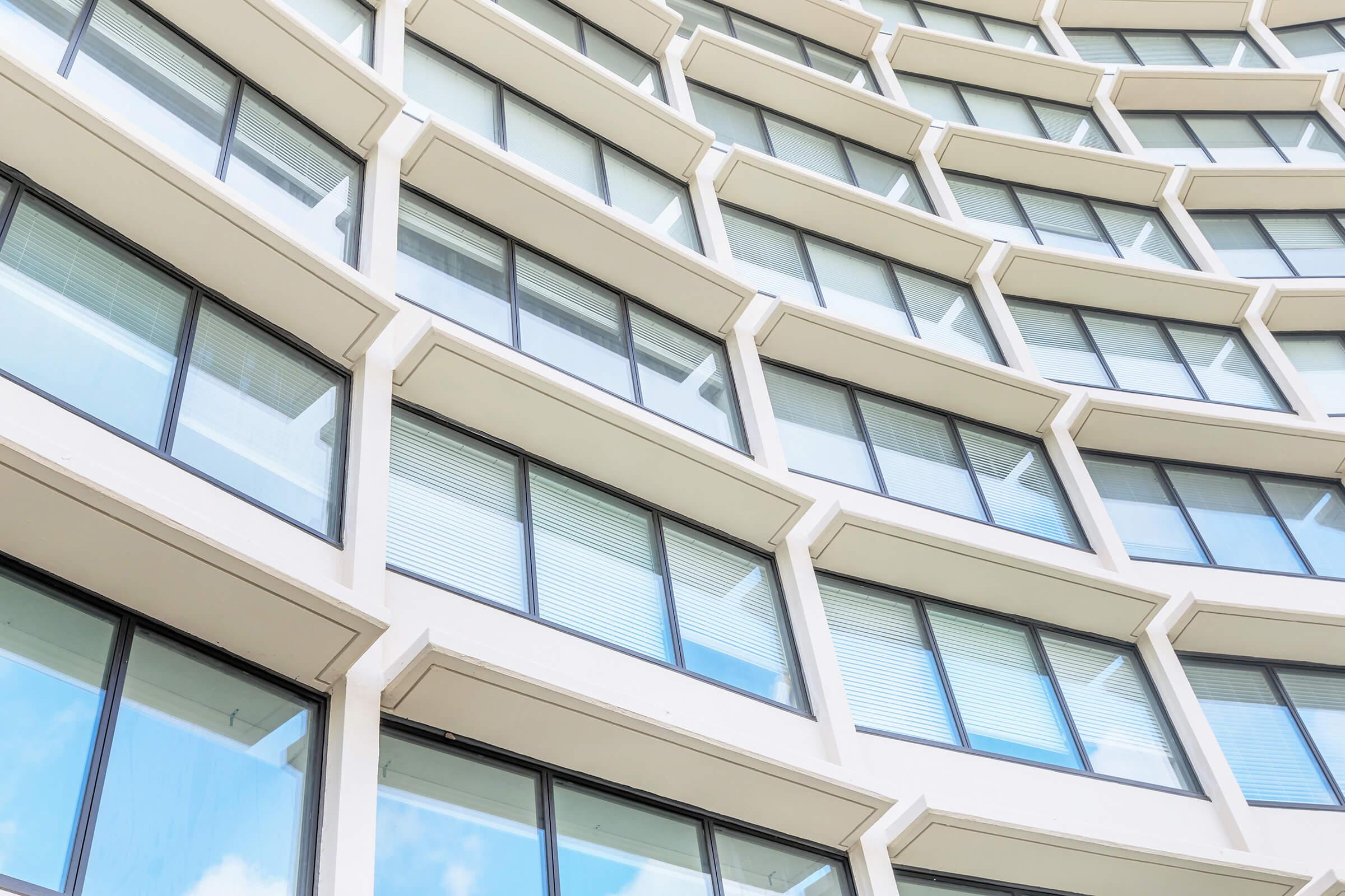 A close-up view of a modern building facade featuring a series of curved windows. The windows have a reflective surface that reflects the sky and surrounding environment. The architectural design emphasizes repeated patterns and a sleek, contemporary aesthetic.