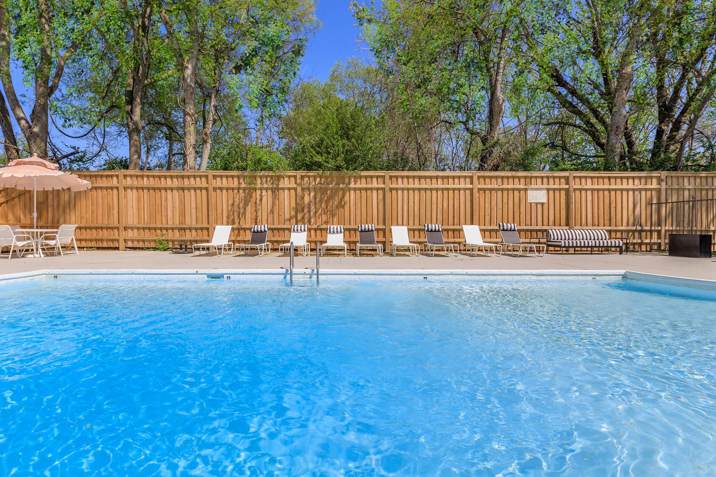 Sparkling swimming pool large deck with many pool chairs.