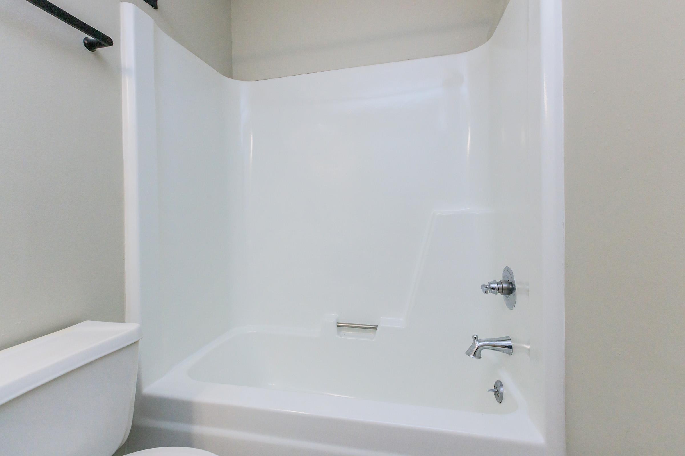 A clean, empty bathroom featuring a white bathtub and shower area, with a modern faucet and a toilet nearby. The walls are painted a light color, creating a bright and spacious appearance.