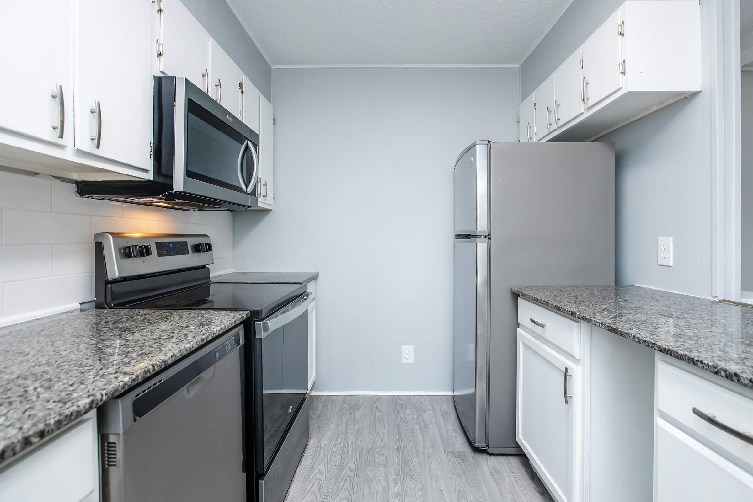 Modern kitchen featuring stainless steel appliances, including an oven, microwave, and refrigerator. The countertops are a dark granite, and the cabinetry is white. The walls are painted a light blue, creating a bright and inviting atmosphere. The flooring is a light wood laminate, enhancing the contemporary look of the space.