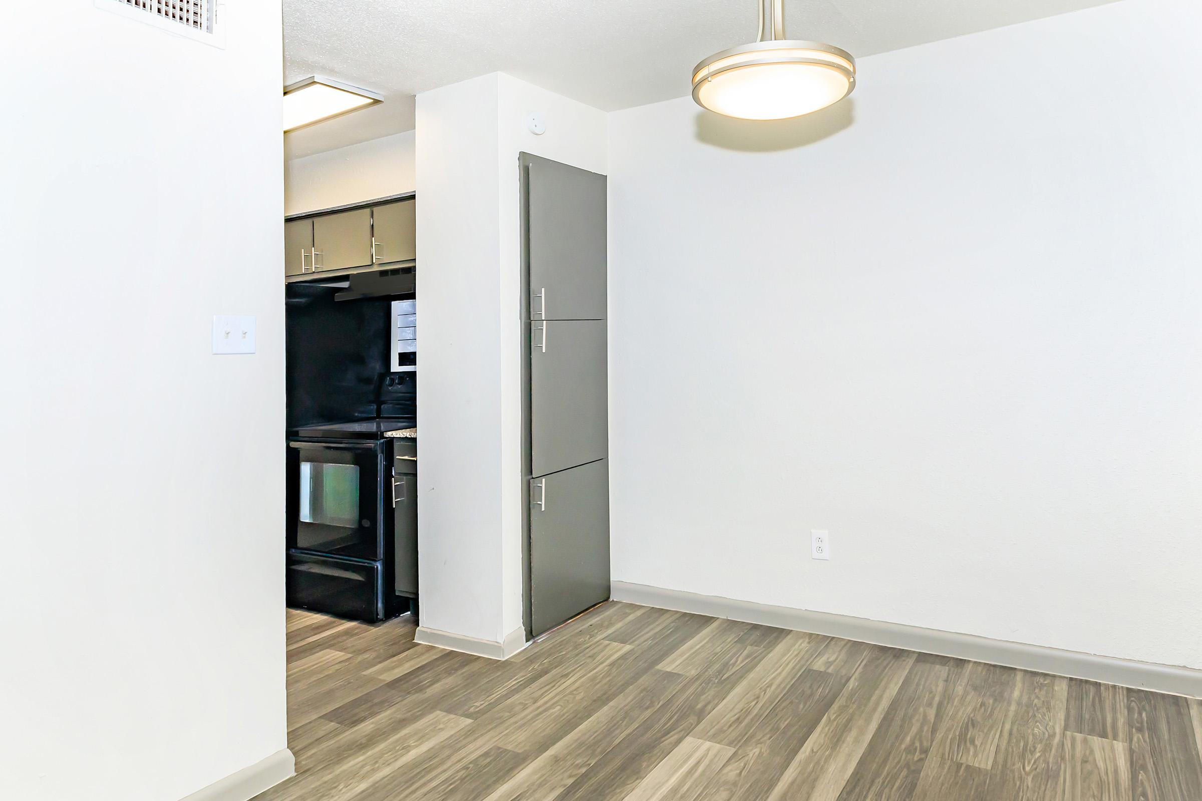 A bright and modern kitchen and living area featuring light-colored walls, laminate flooring, and a contemporary ceiling light fixture. The kitchen has sleek cabinets and appliances, while the space is clean and inviting, designed for comfort and style in an apartment setting.