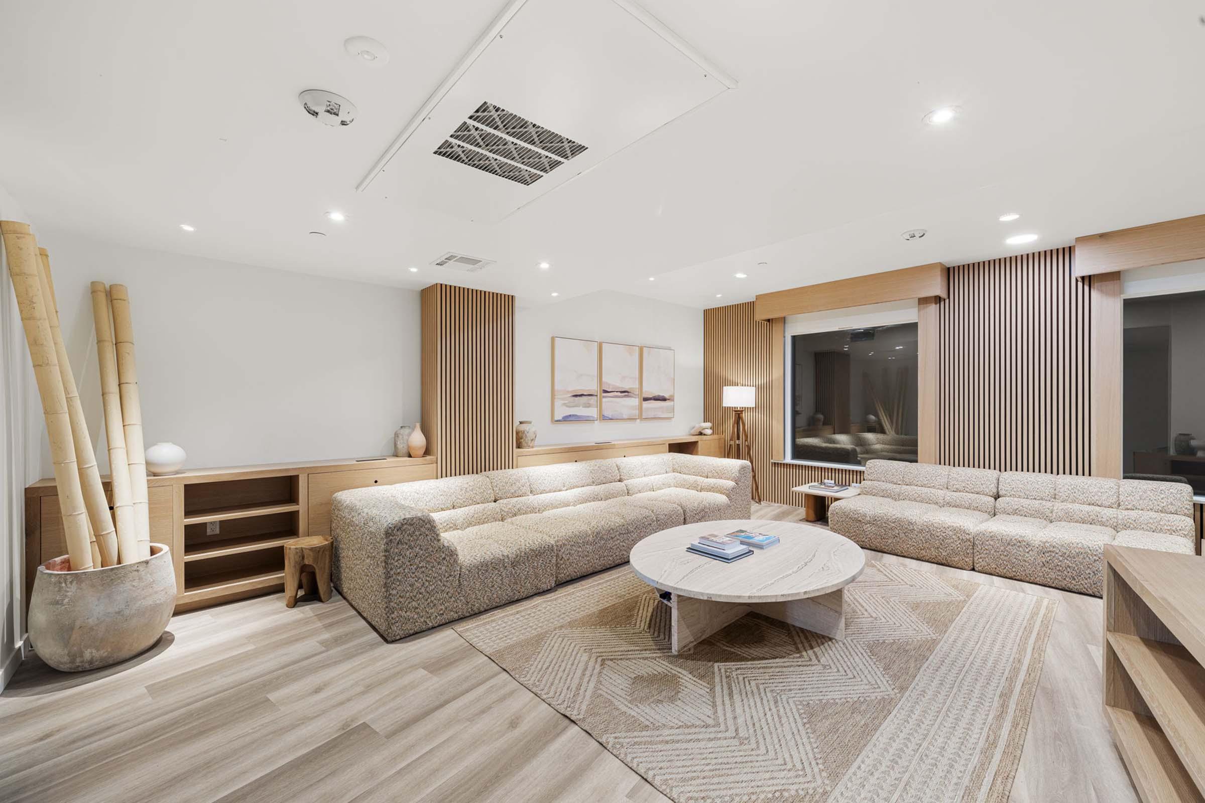 A modern living room featuring two stylish sofas arranged around a round coffee table. The space includes wood paneling, a neutral color palette, and decorative elements like a plant and artwork on the walls. Soft lighting enhances the cozy atmosphere.