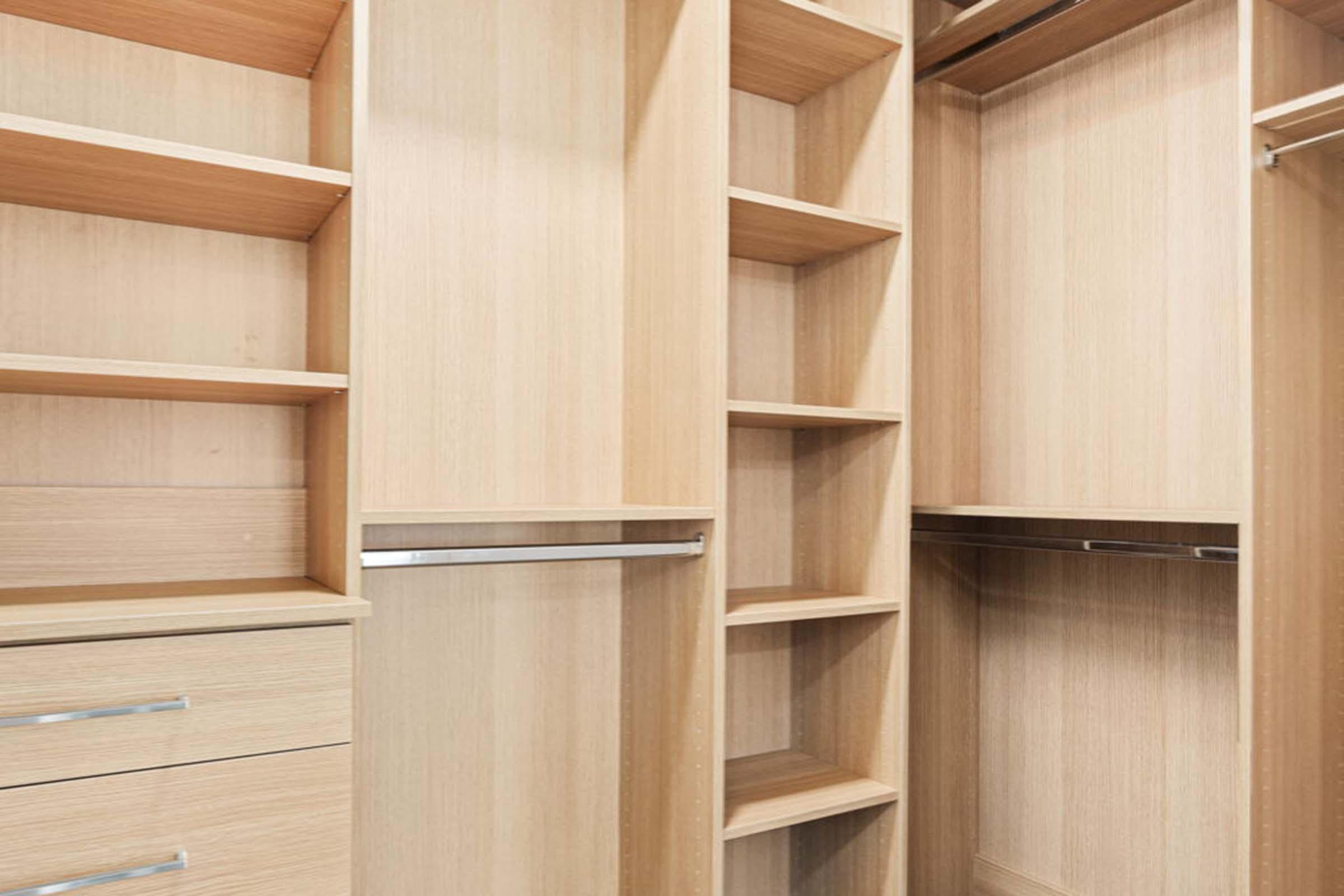 Empty wooden closet with various shelving and drawer sections, featuring a light wood finish. The design includes open shelves, a hanging rod, and a few compartments for storage, creating a spacious and organized look.