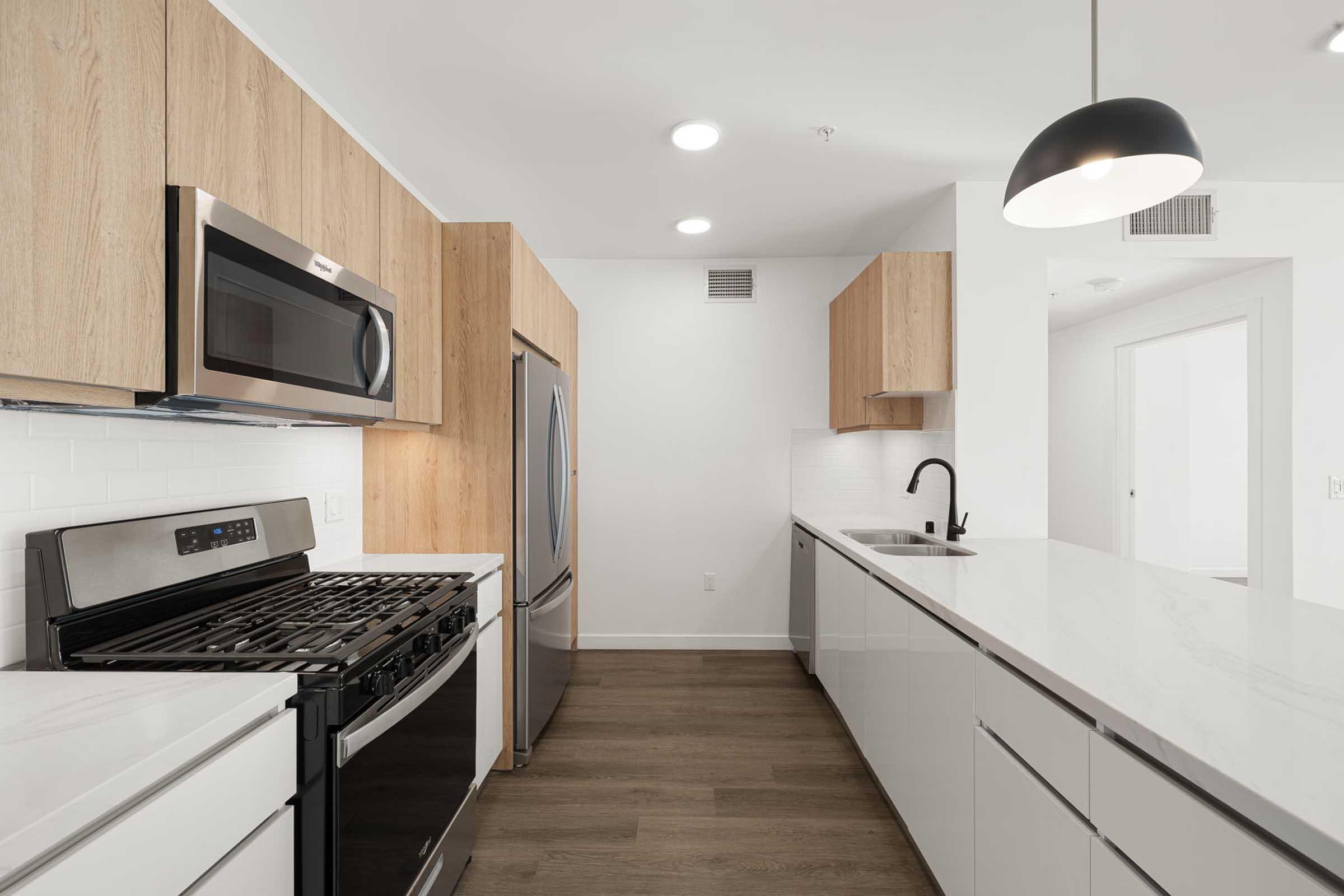 Modern kitchen featuring stainless steel appliances, including a gas stove and refrigerator. The cabinetry combines light wood and sleek white finishes, with a minimalist design. Bright, natural light illuminates the space, highlighting the clean, contemporary aesthetic.