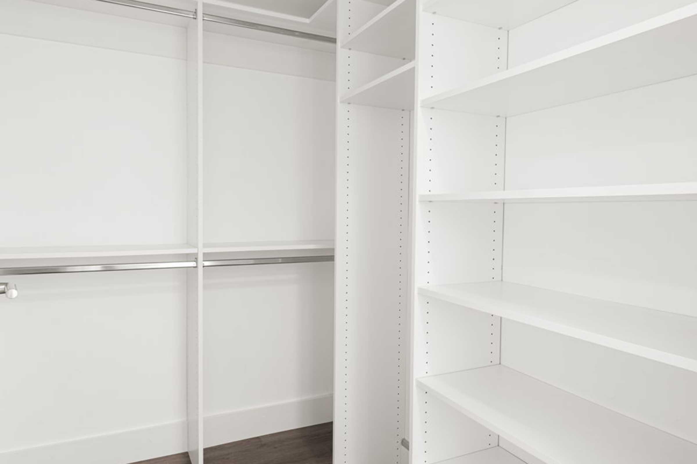 An empty white closet featuring open shelves, a hanging rod, and a minimalist design. The walls are clean and bright, emphasizing the spaciousness and organization of the storage area.