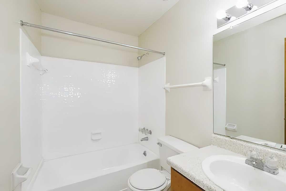 A clean and modern bathroom featuring a white bathtub with a sliding shower door, a countertop with a sink, a mirror above the sink, and light fixtures overhead. The walls are painted a neutral color, and the space is well-lit and organized.