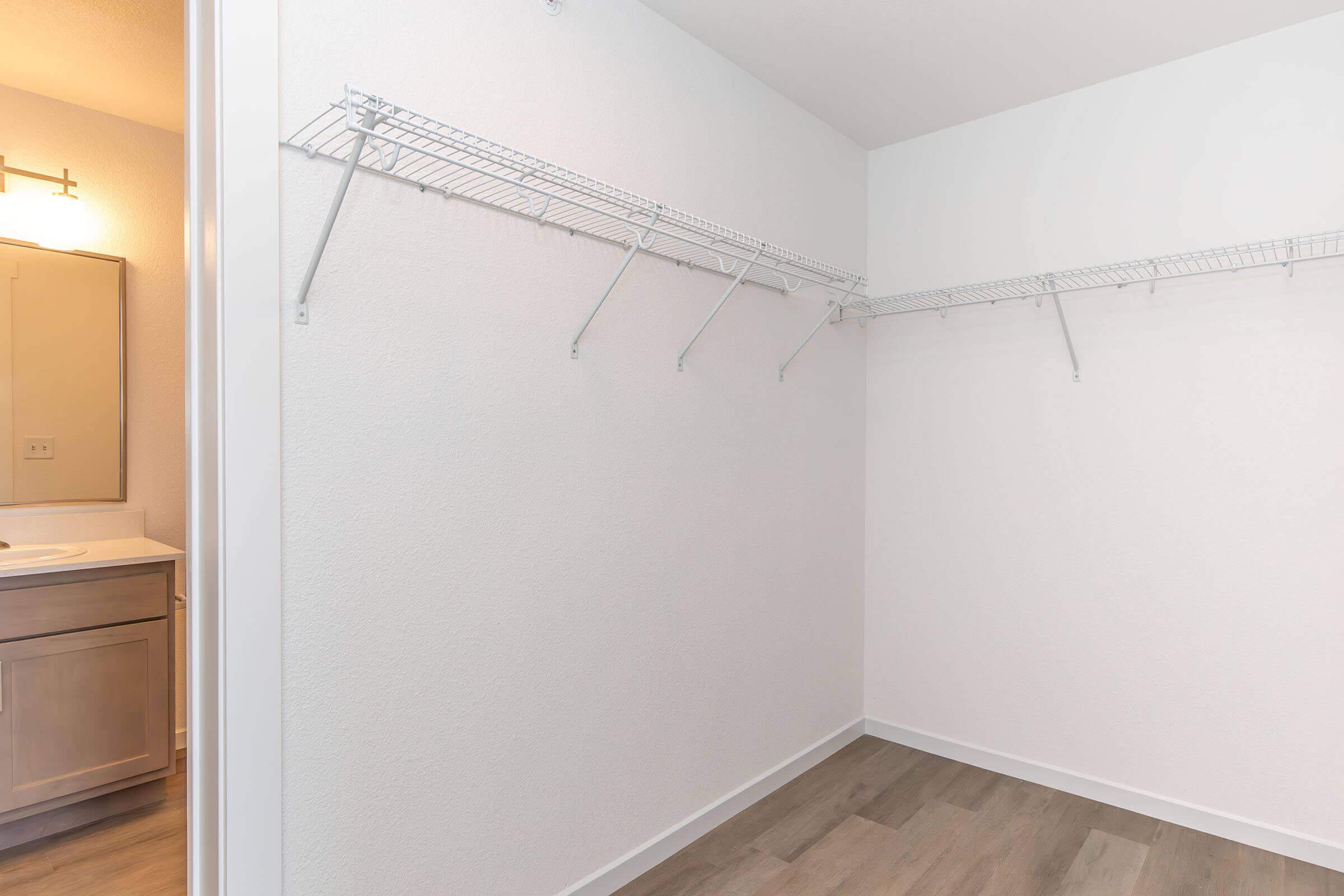 Empty closet featuring wire shelving on two walls, with light-colored walls and hardwood flooring. A bathroom vanity is partially visible in the background, suggesting a well-lit space. The room is clean and uncluttered, ideal for storage.