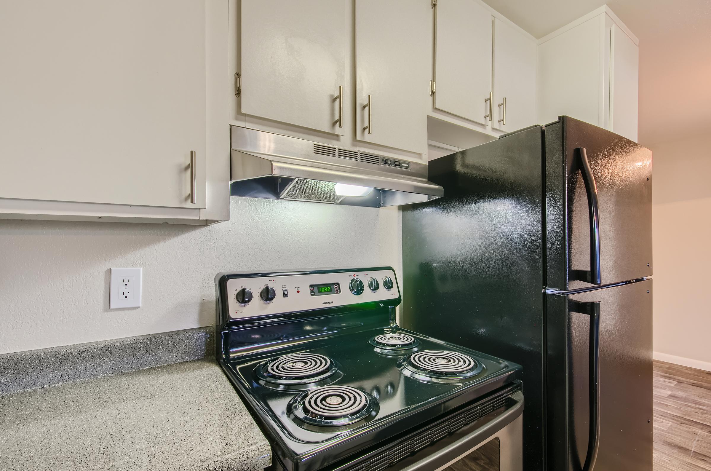An apartment kitchen at Rise on McClintock with white cabinets and black appliances.